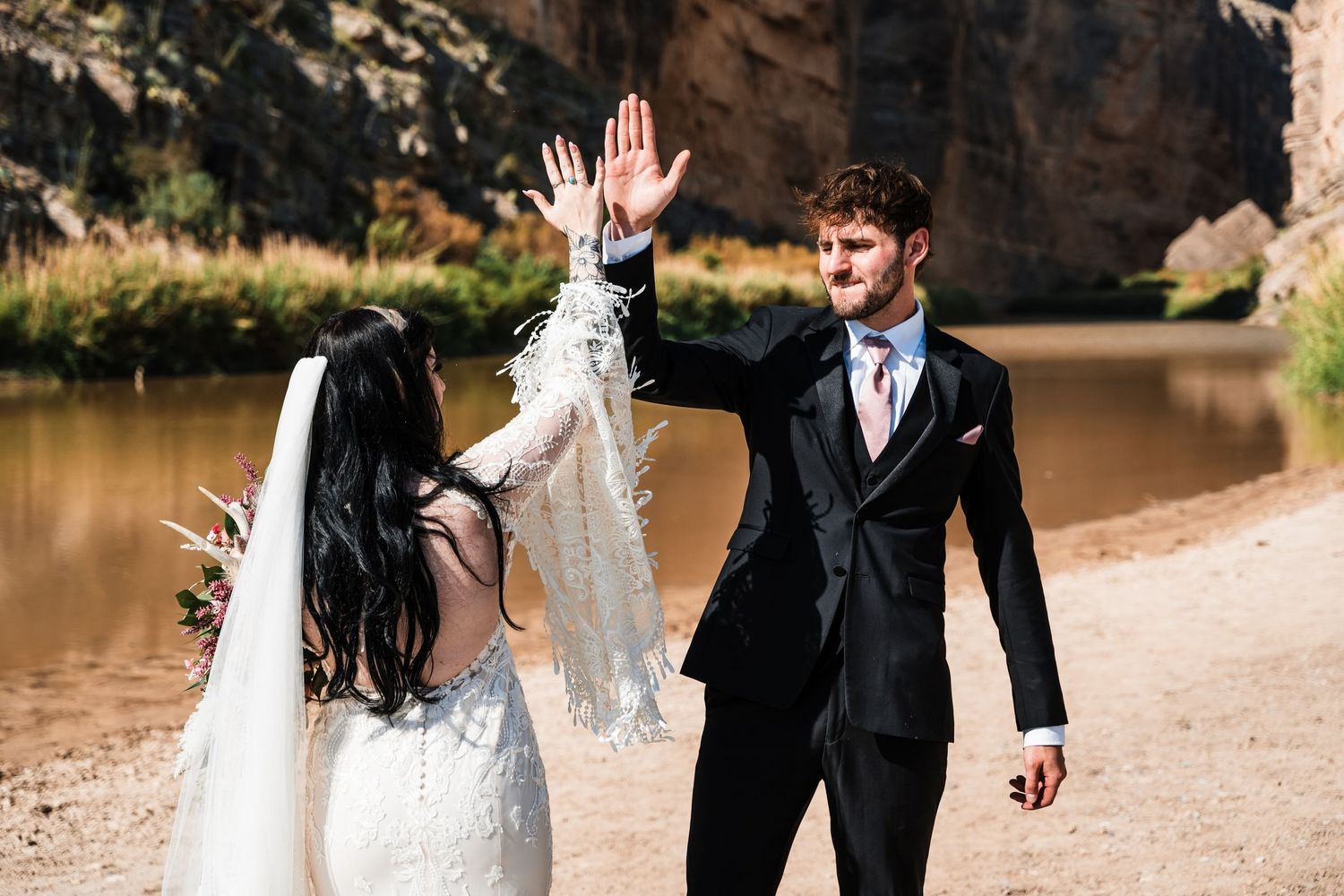 Happy couple sharing a joyful high-five moment during their desert wedding photoshoot.