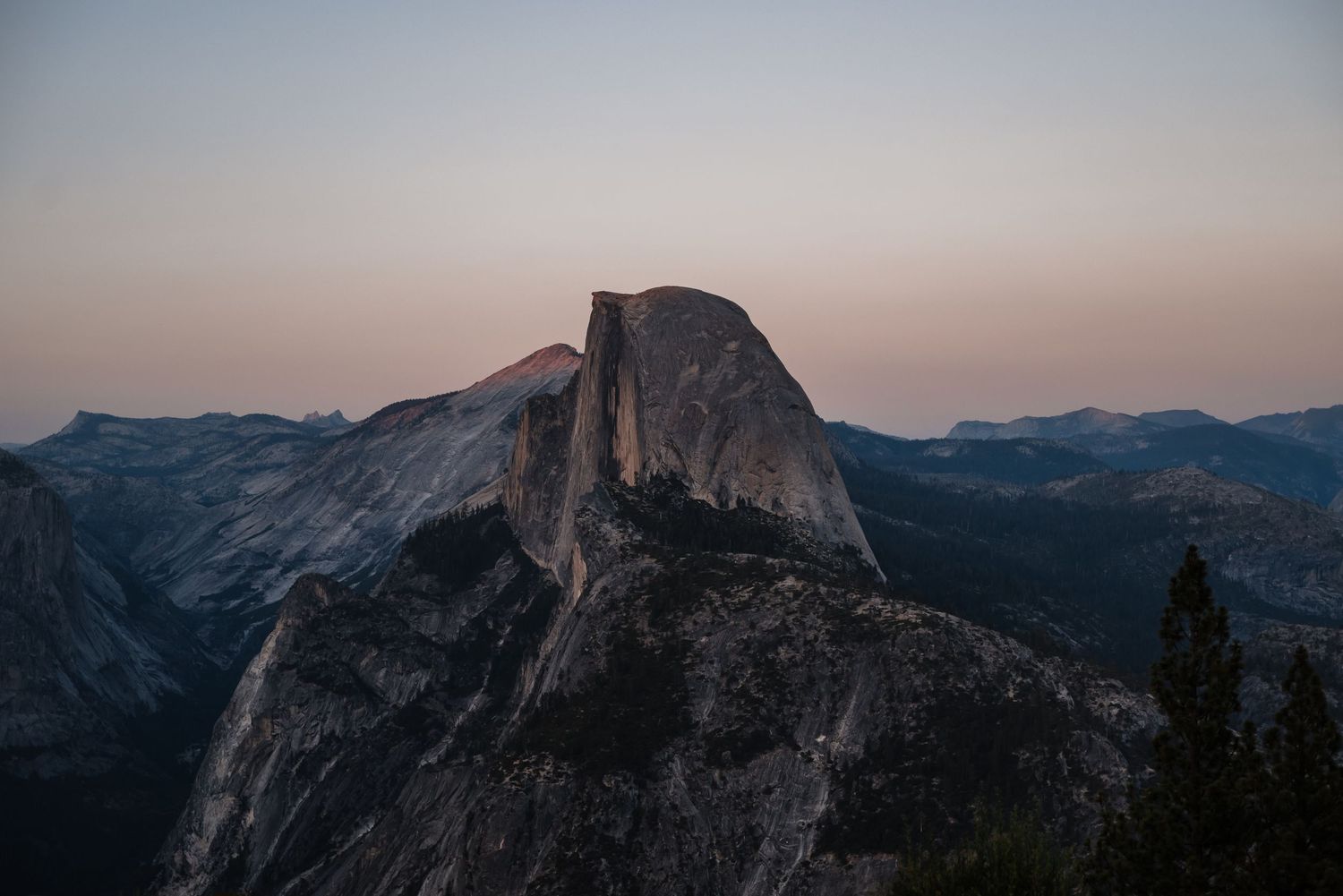 Panoramic view of Half Dome and Yosemite Valley mountains at dusk.
