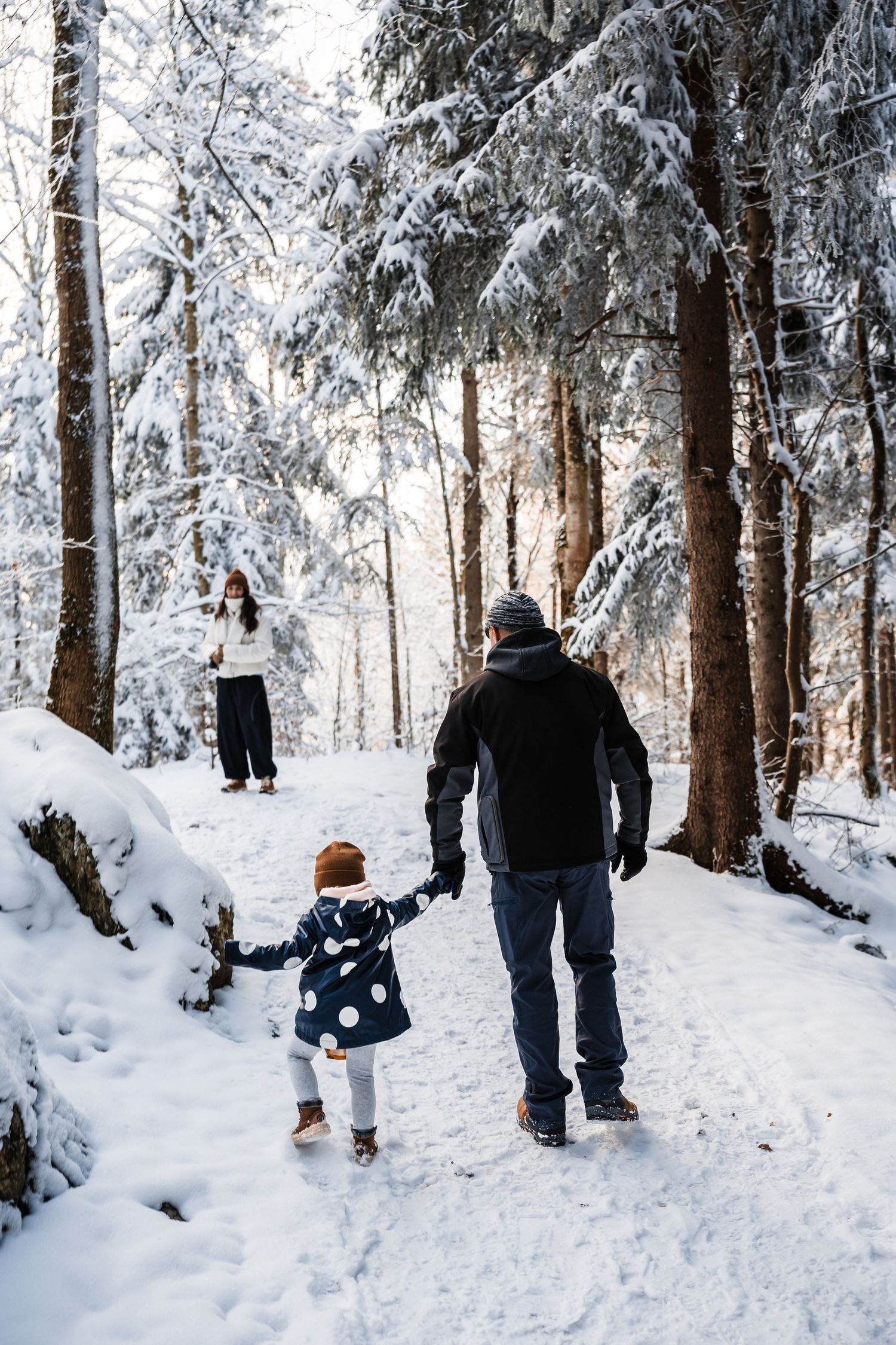 Family walking together on a snow-covered forest trail surrounded by frost-covered evergreen trees.