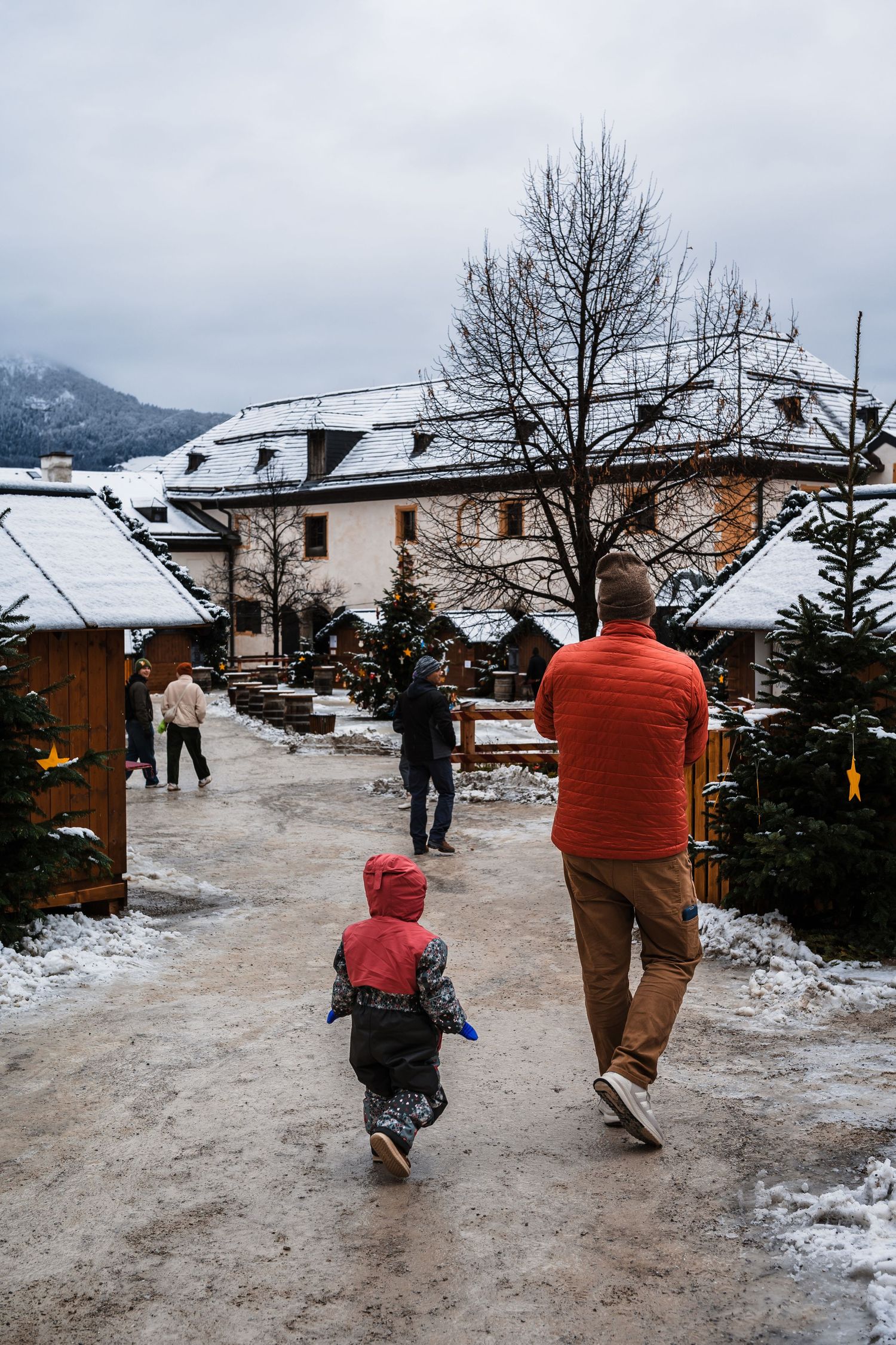 People walking on a snowy path between buildings in a winter mountain village setting.