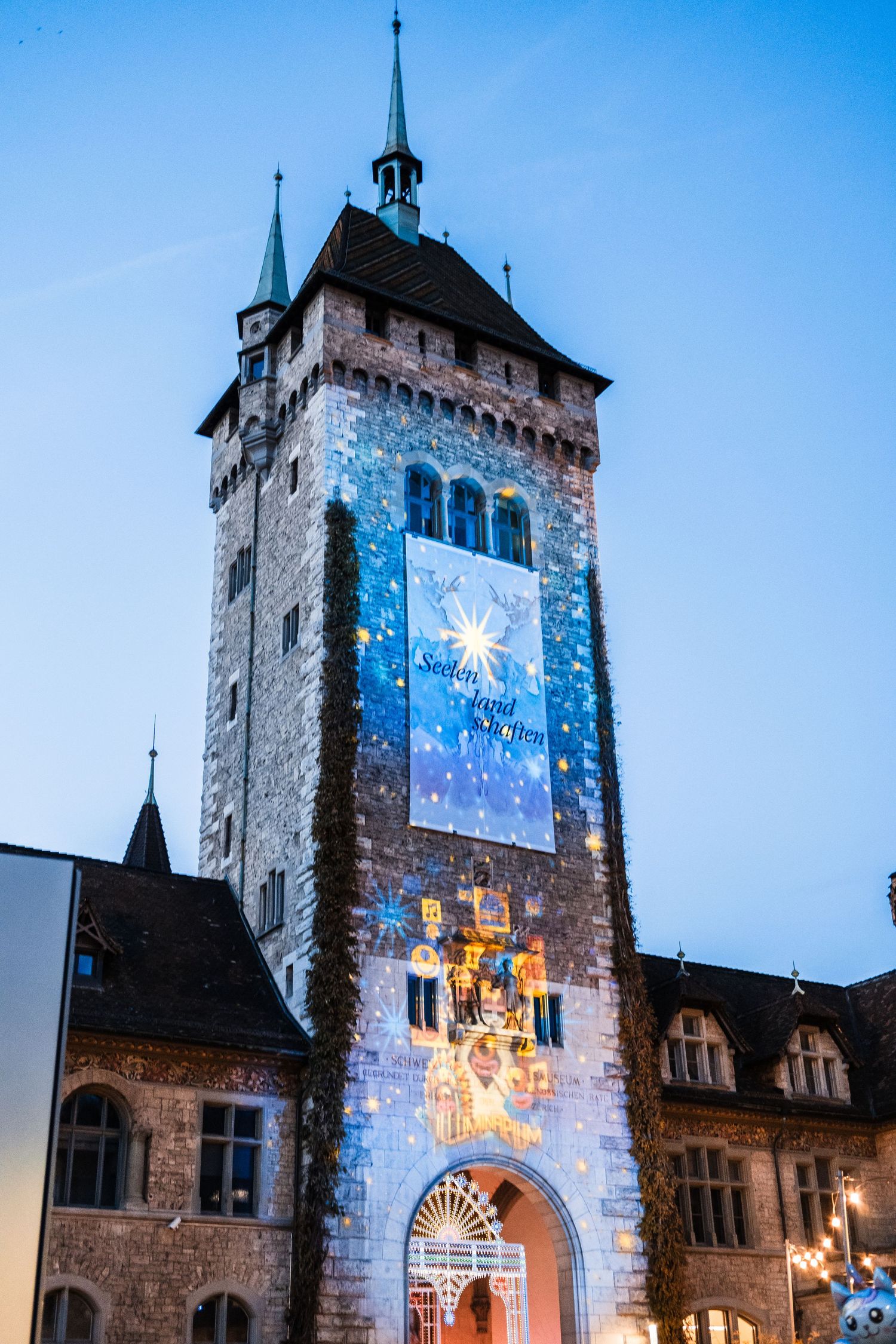 Historic stone tower illuminated with festive winter projections showing snowflakes and holiday scenes at dusk.