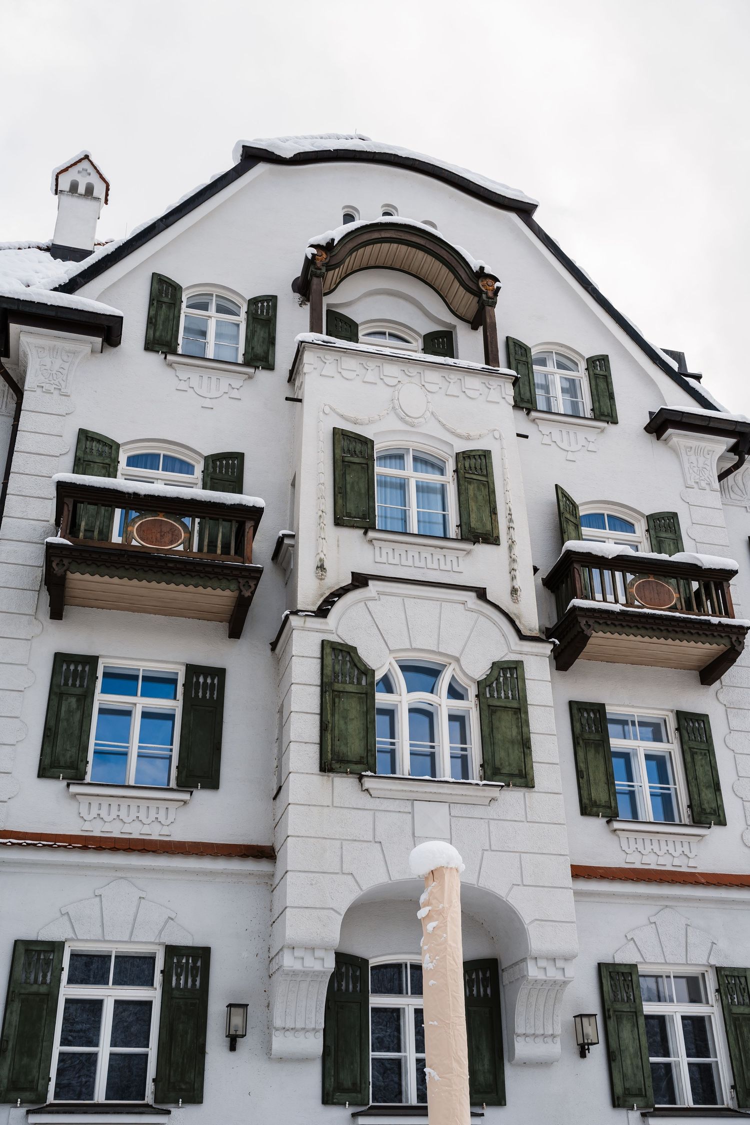 White European-style building facade with green shutters and ornate architectural details against a bright sky.