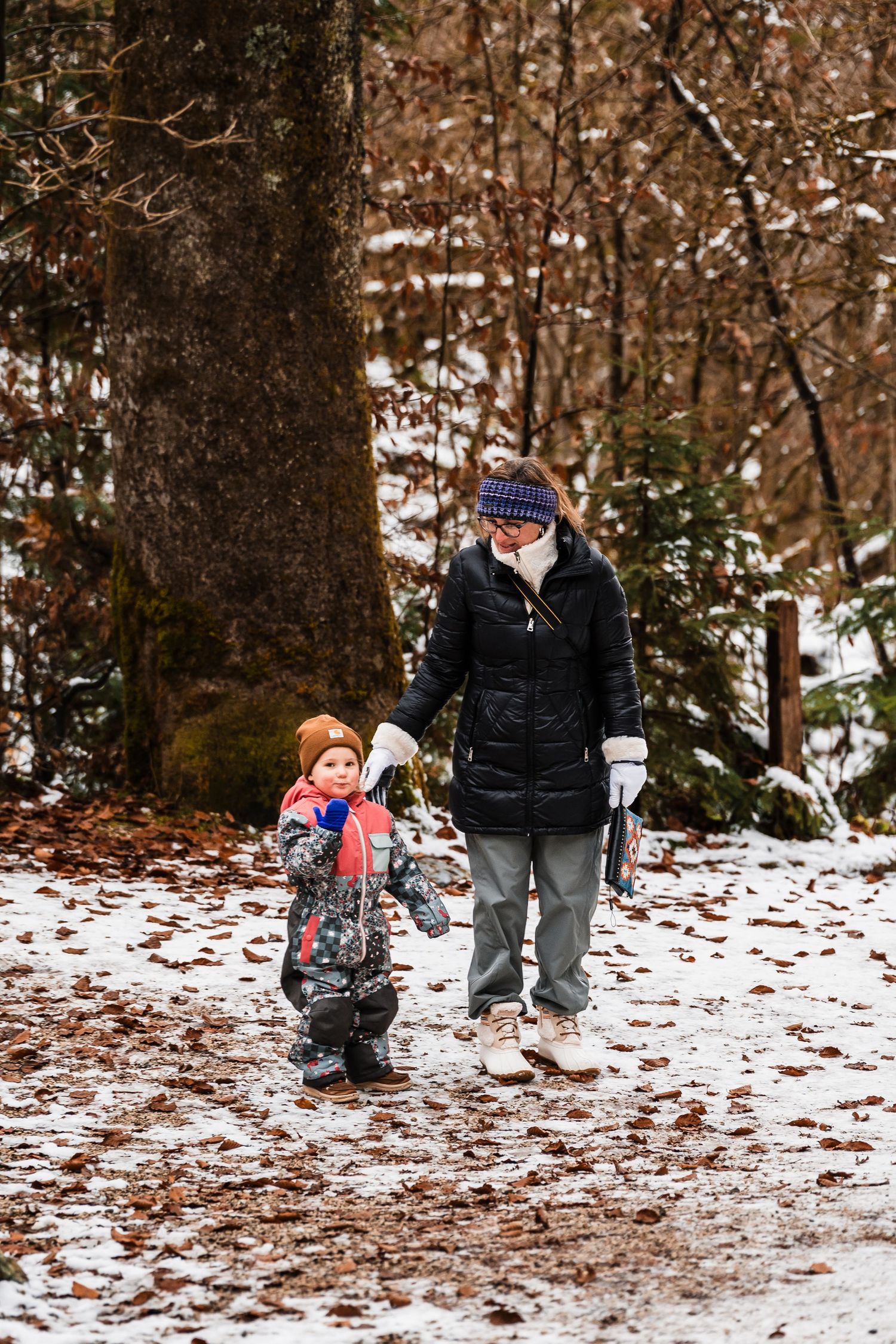 Two people walking together on a snowy forest trail during winter while wearing warm coats and winter accessories.