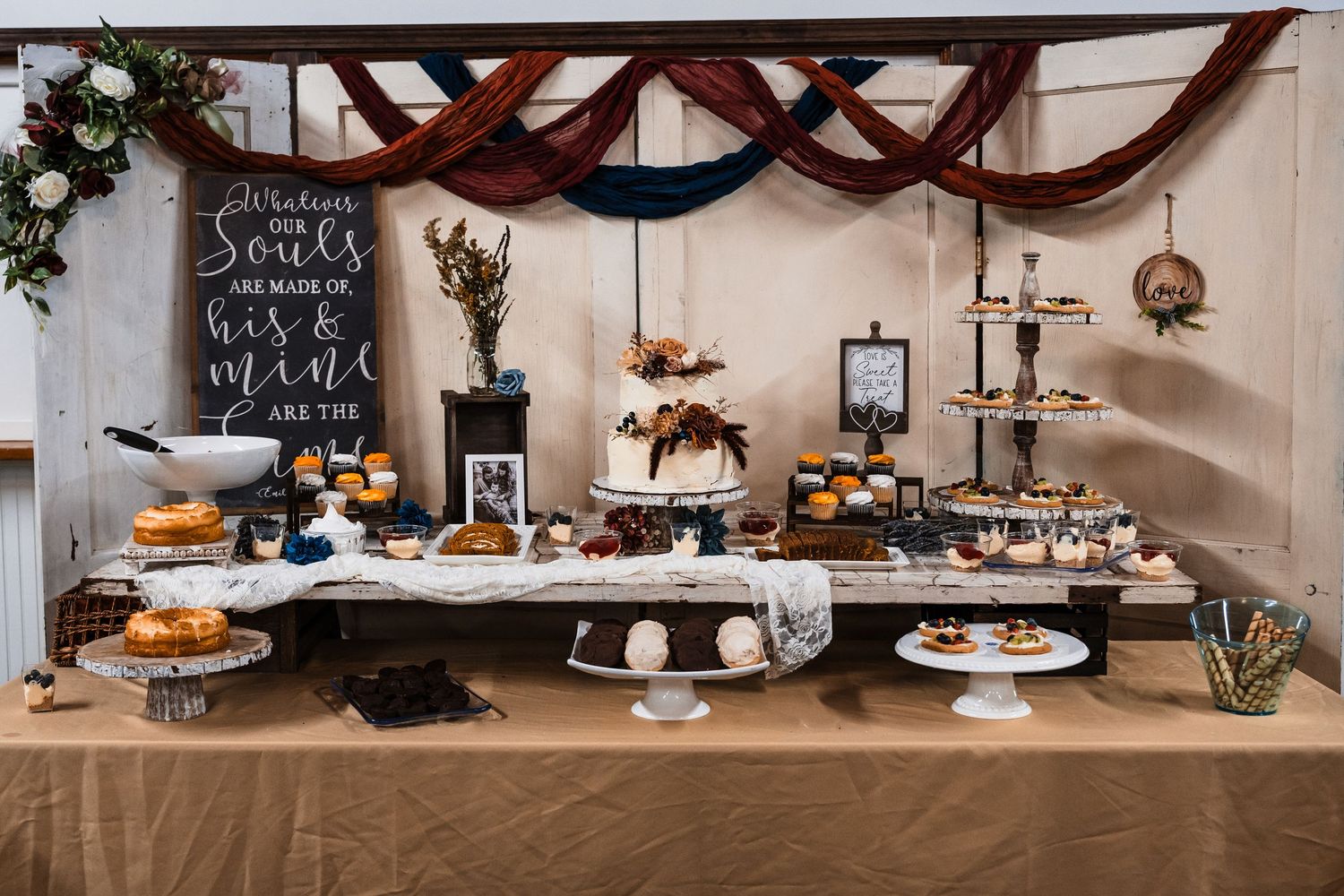 Long rustic wedding dessert display table with cakes and treats decorated in autumn colors.