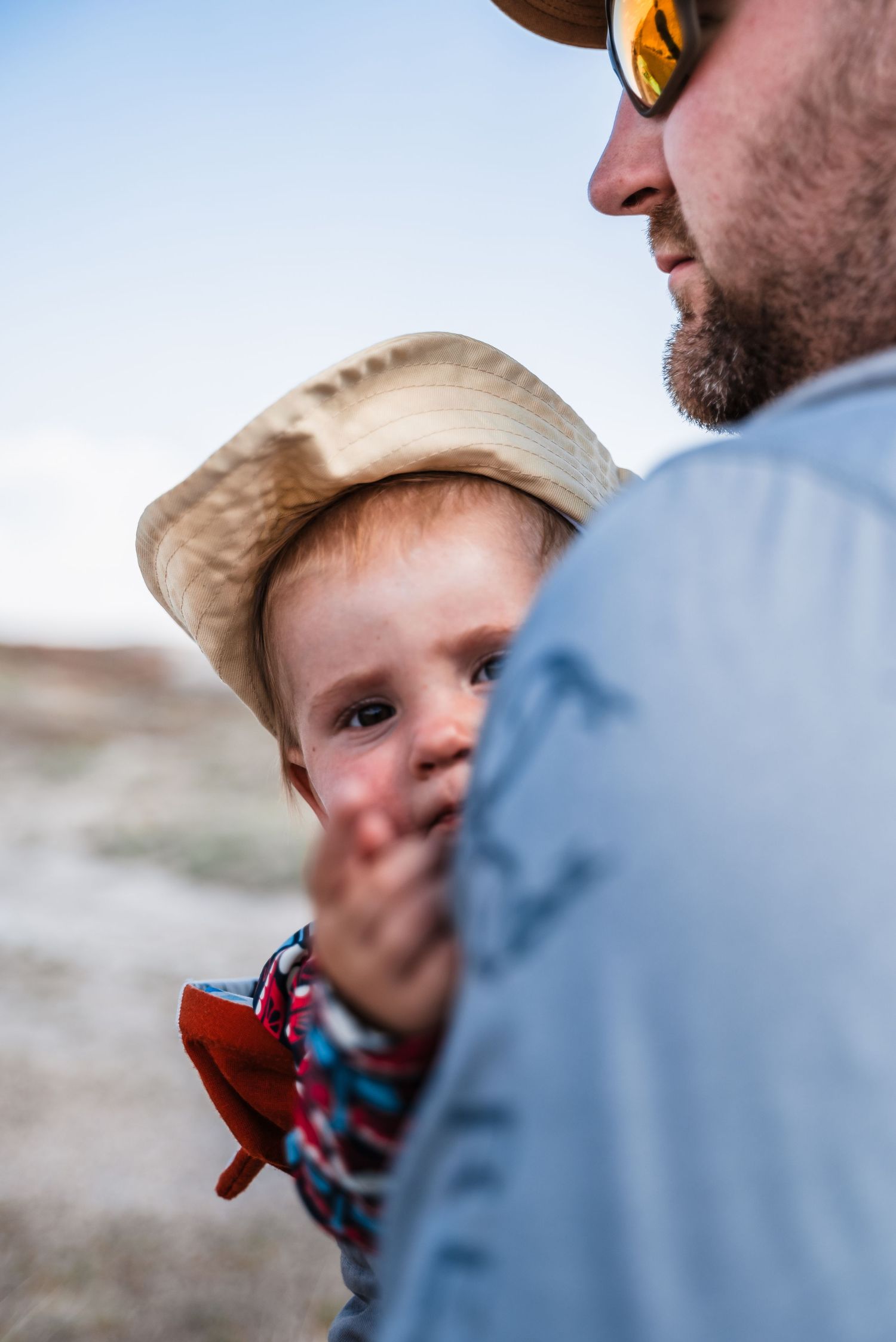 A candid outdoor portrait showing a close-up view in sunlight with reflective sunglasses and a tan hat.