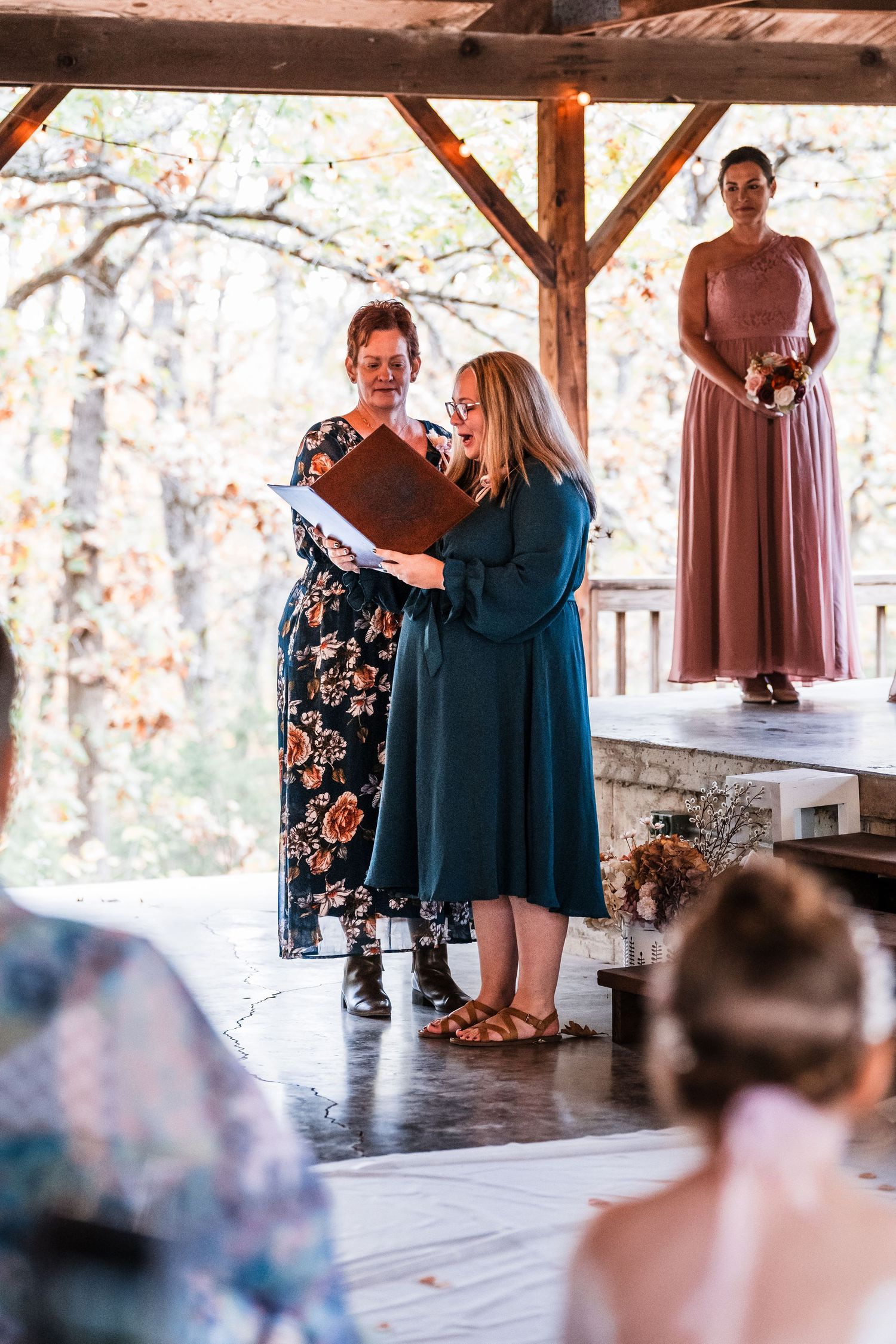 Wedding guests gather under a covered outdoor venue with natural lighting and wooden beams.