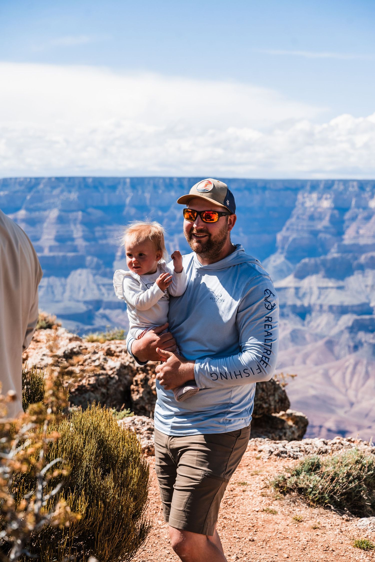 Visitors enjoy scenic views at the Grand Canyon rim on a sunny day with white clouds in the blue sky.