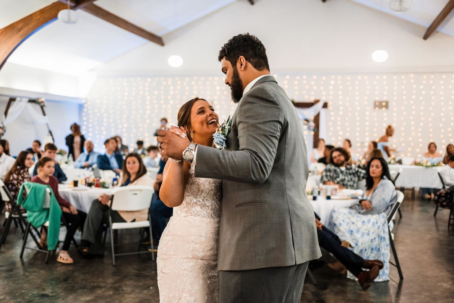 Newlyweds share their first dance together in a reception hall with guests watching in the background.