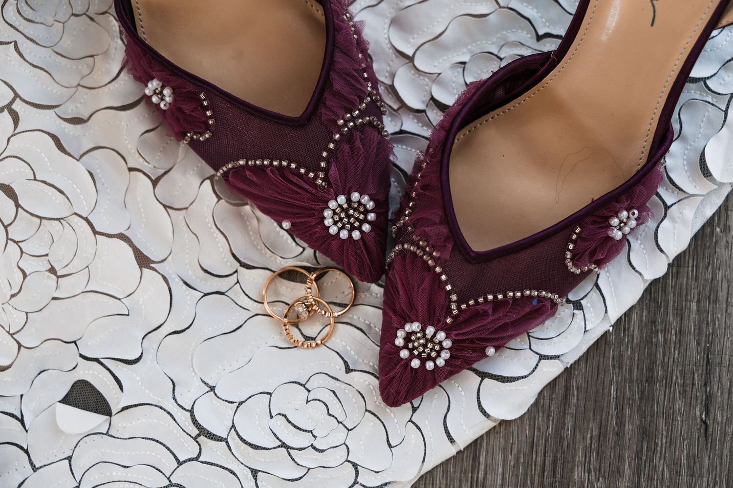 Close-up of burgundy dress shoes with crystal embellishments on a textured white surface.