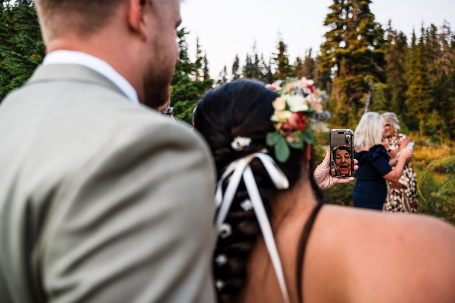 Wedding ceremony gathering surrounded by evergreen trees and mountain scenery.