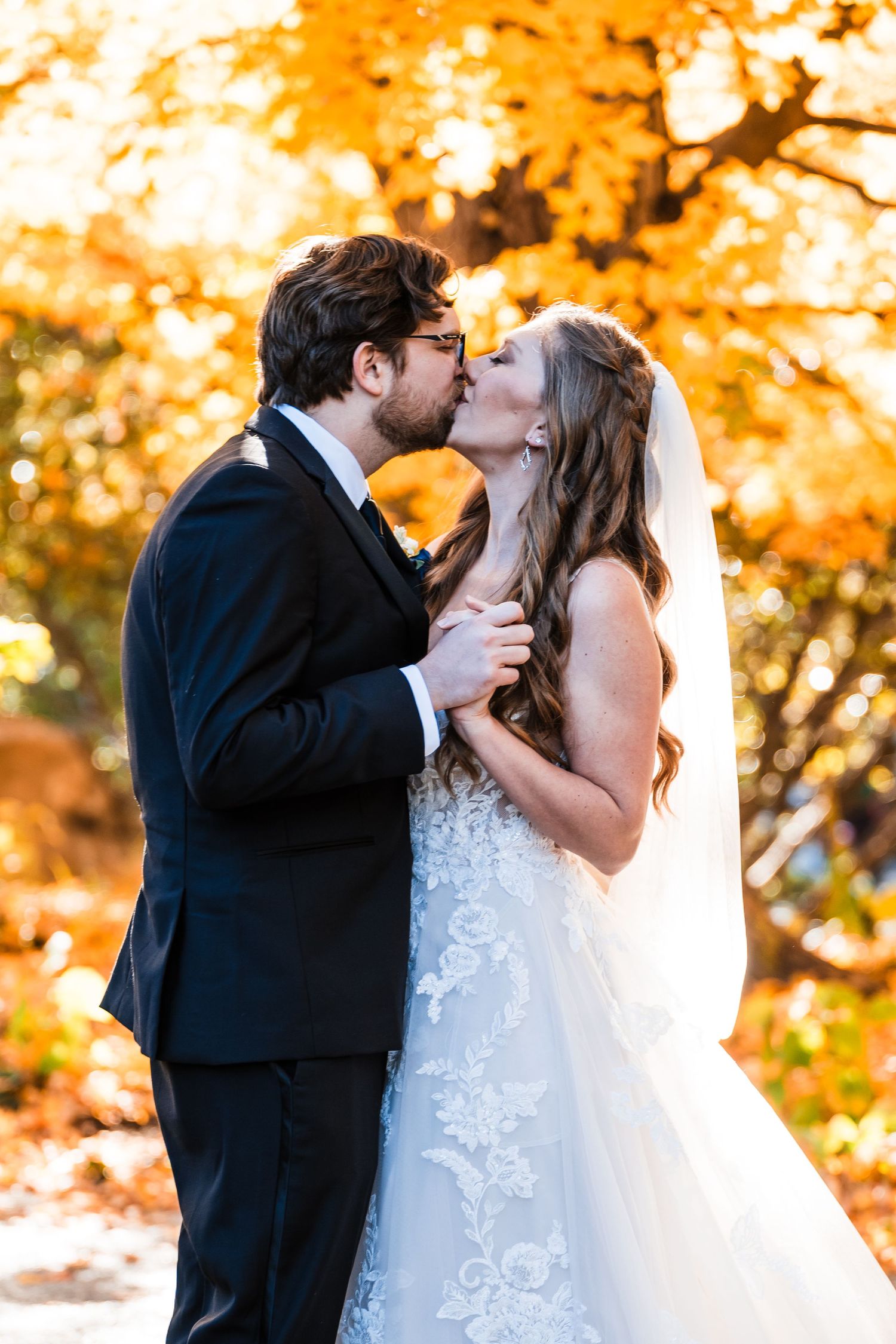 Romantic kiss between newlyweds with vibrant orange fall foliage backdrop.