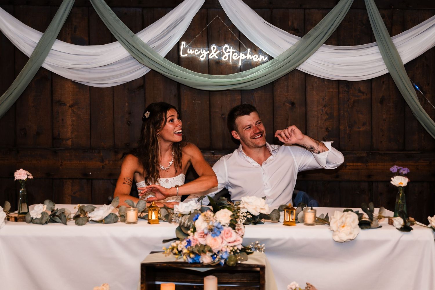 Newlyweds sharing a candid moment at their reception table under elegant draping.
