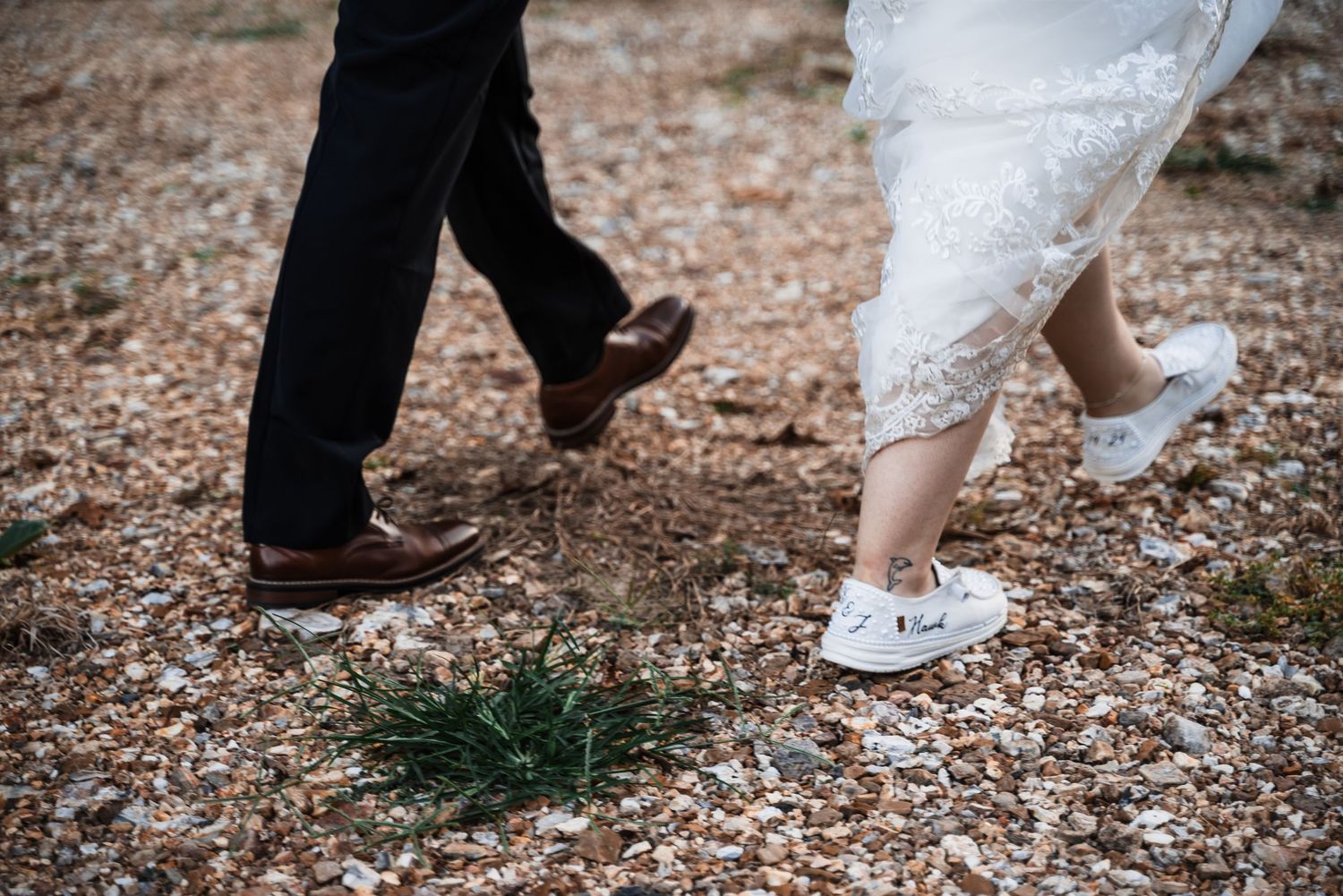 Close-up of bride and groom's feet walking together on gravel path.