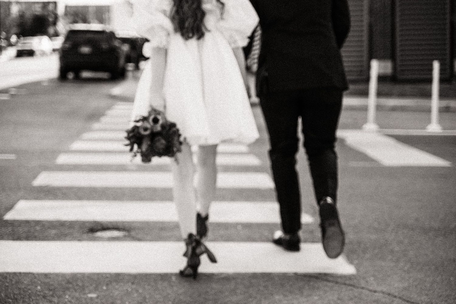 Black and white photo of a couple's legs walking across a crosswalk, showing dress and formal shoes.