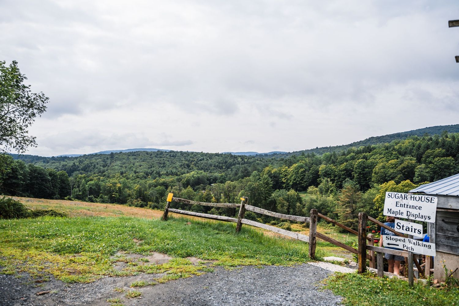 A scenic overlook with wooden fence and directional signs overlooking green rolling hills and forest in the distance.