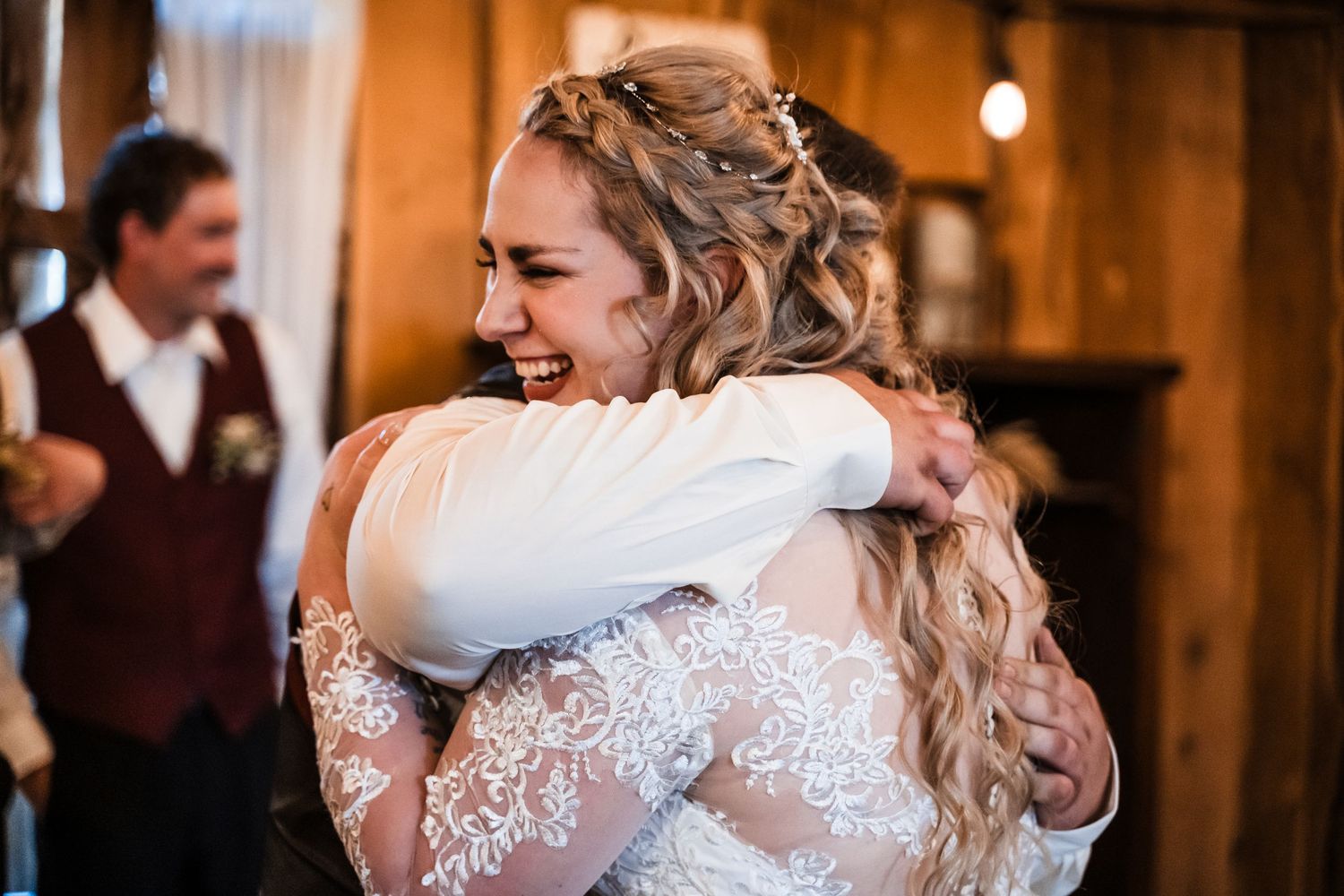 A happy couple embraces during a wedding celebration in a rustic indoor venue with wood paneling and warm lighting.