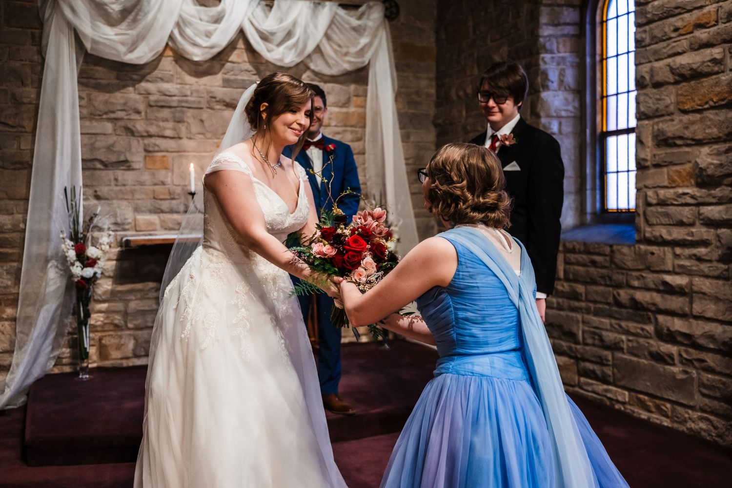 Wedding ceremony in stone church with draped fabric arch and blue bridesmaid dress.