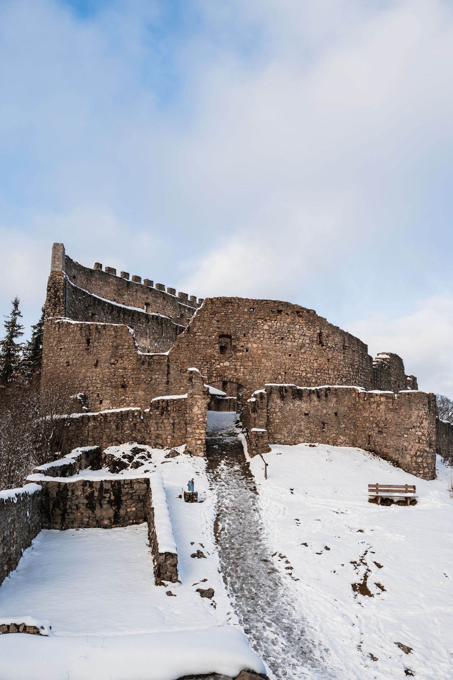 Ancient stone castle ruins covered in snow against a bright blue winter sky.