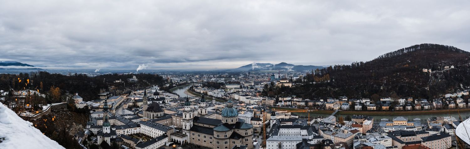 Panoramic winter cityscape view of snow-covered buildings nestled in mountainous terrain.