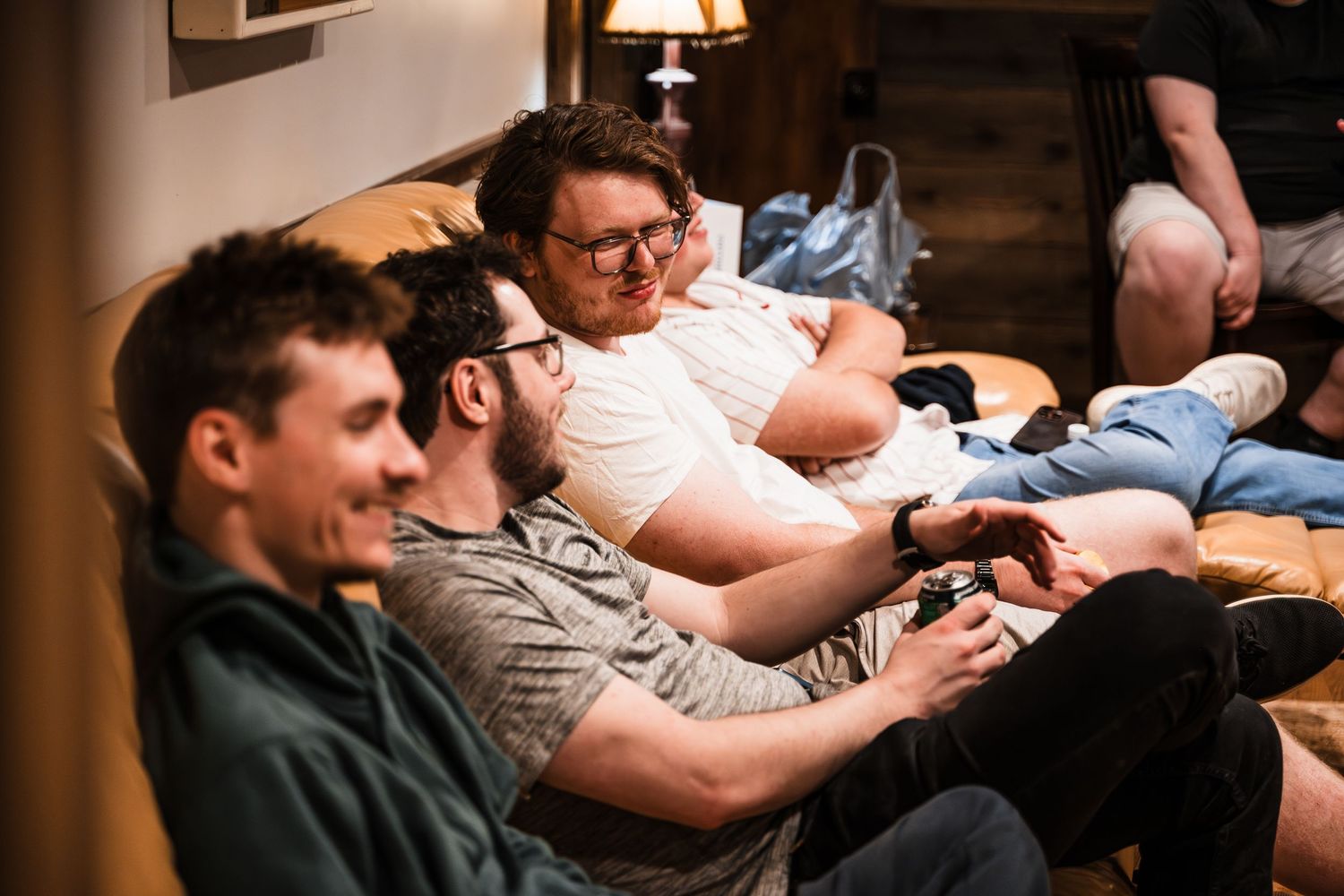 Group of young men sitting together on a couch laughing and playing video games in a cozy room.