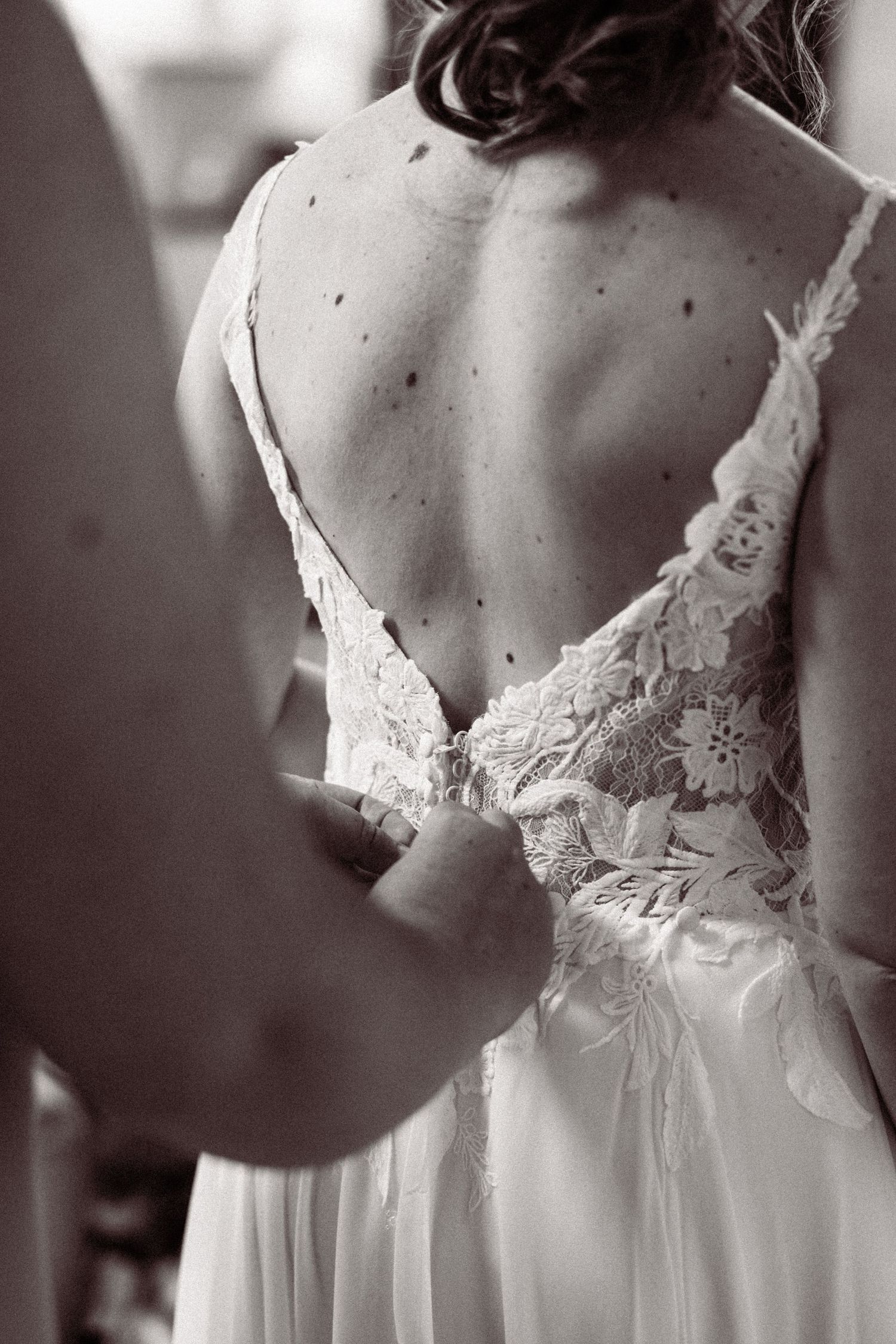 Black and white photo of bride in elegant backless lace wedding gown being fastened.