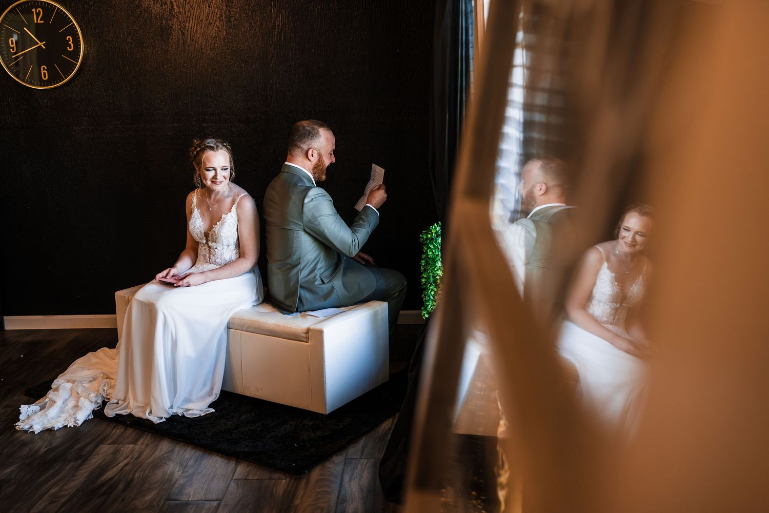 Bride and groom share a private moment seated together in a dimly lit room.