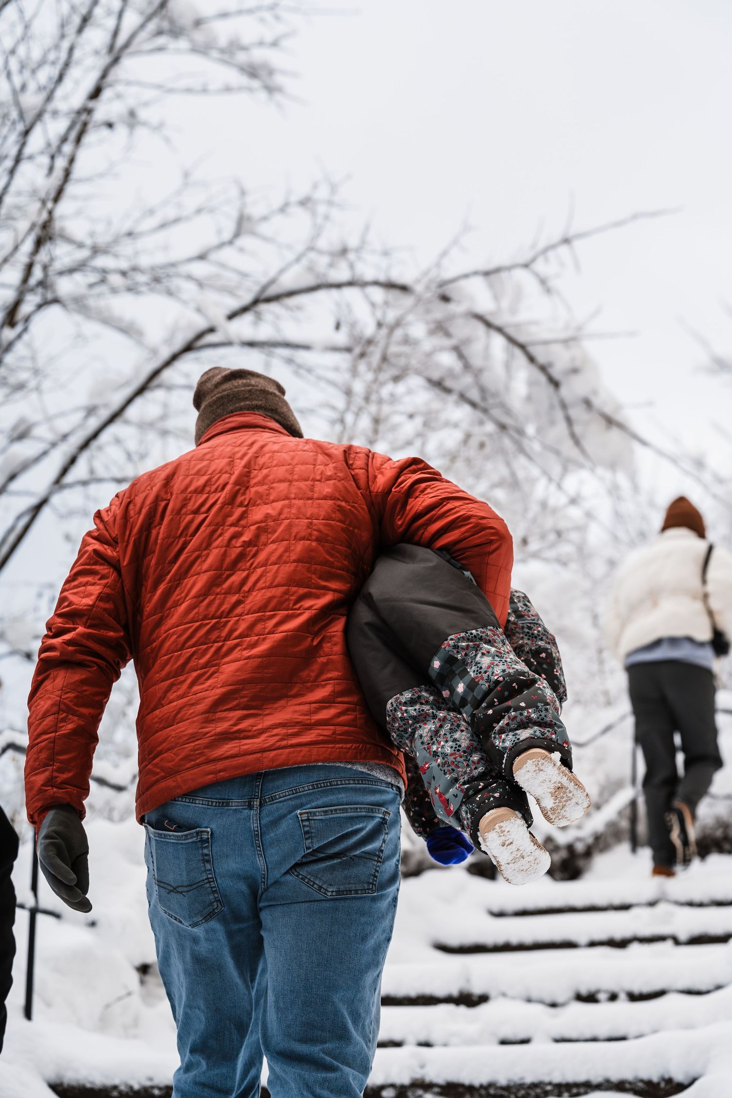 Person in red quilted jacket and jeans bends down to make a snowball in snowy winter landscape.