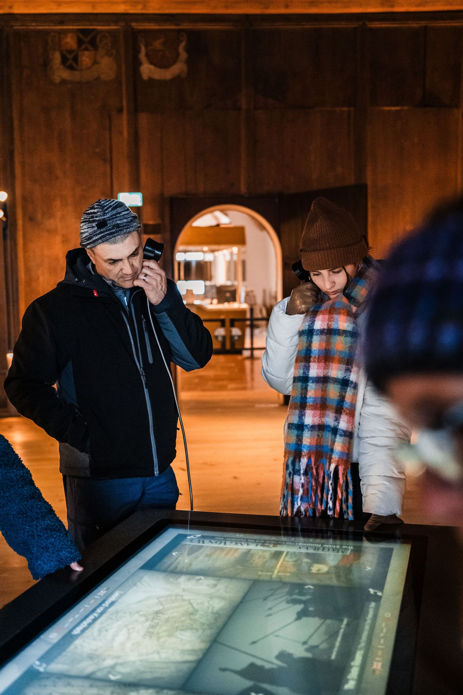 People examining an interactive display screen in a dimly lit museum or exhibit space.