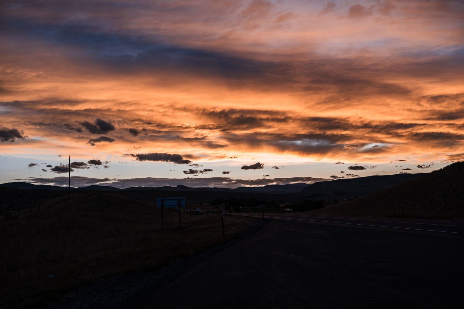 Dramatic orange and purple sunset sky over dark mountain silhouettes with wispy clouds stretching across the horizon.