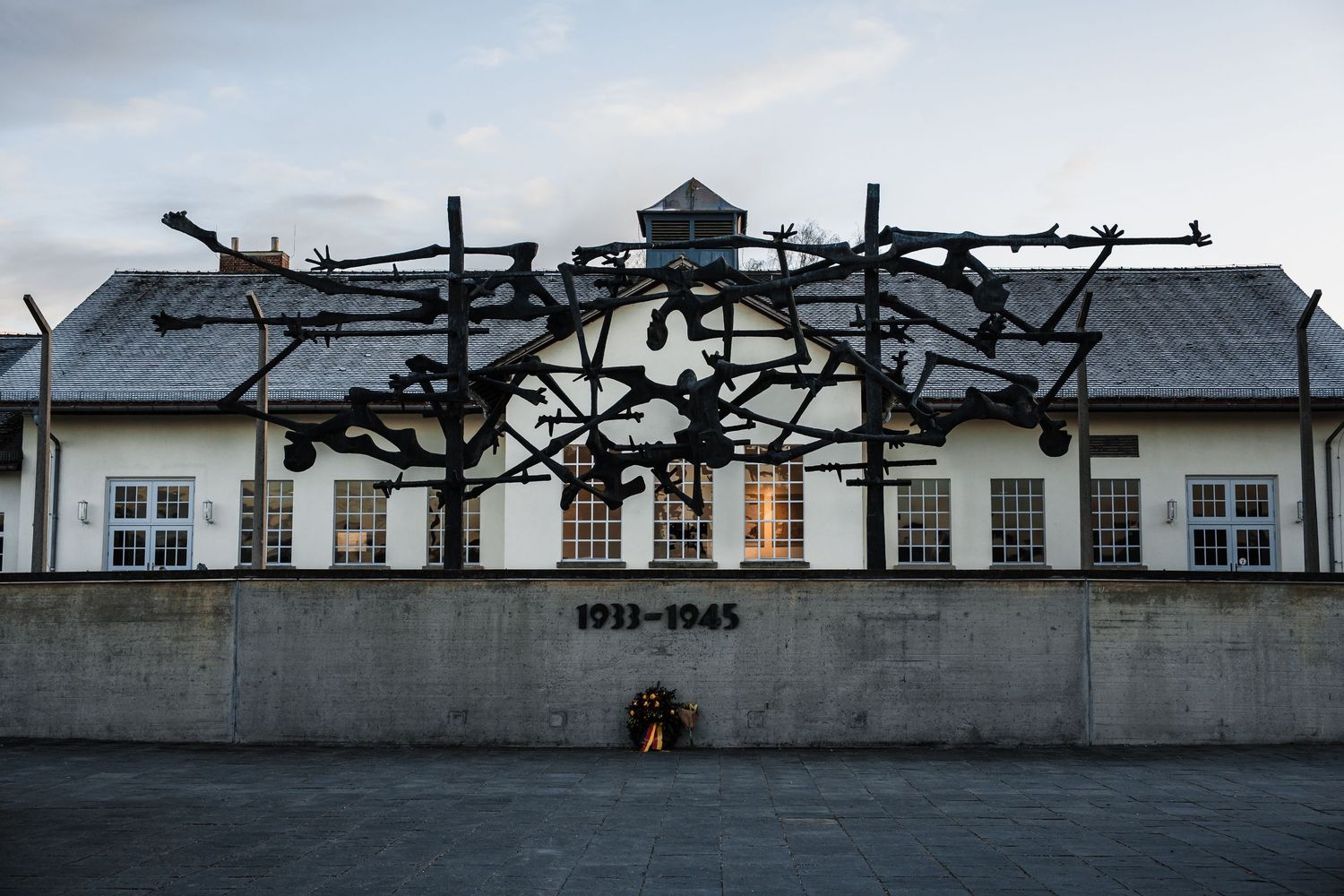 Row of white buildings with damaged roofs at a former concentration camp memorial site at sunset.