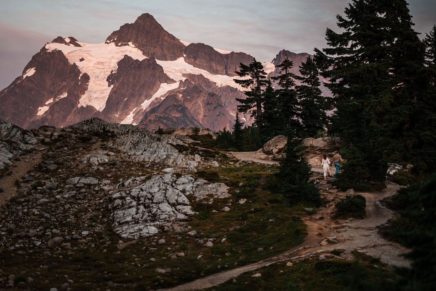 Majestic Mount Baker rises above evergreen trees in Washington State during a colorful sunset.