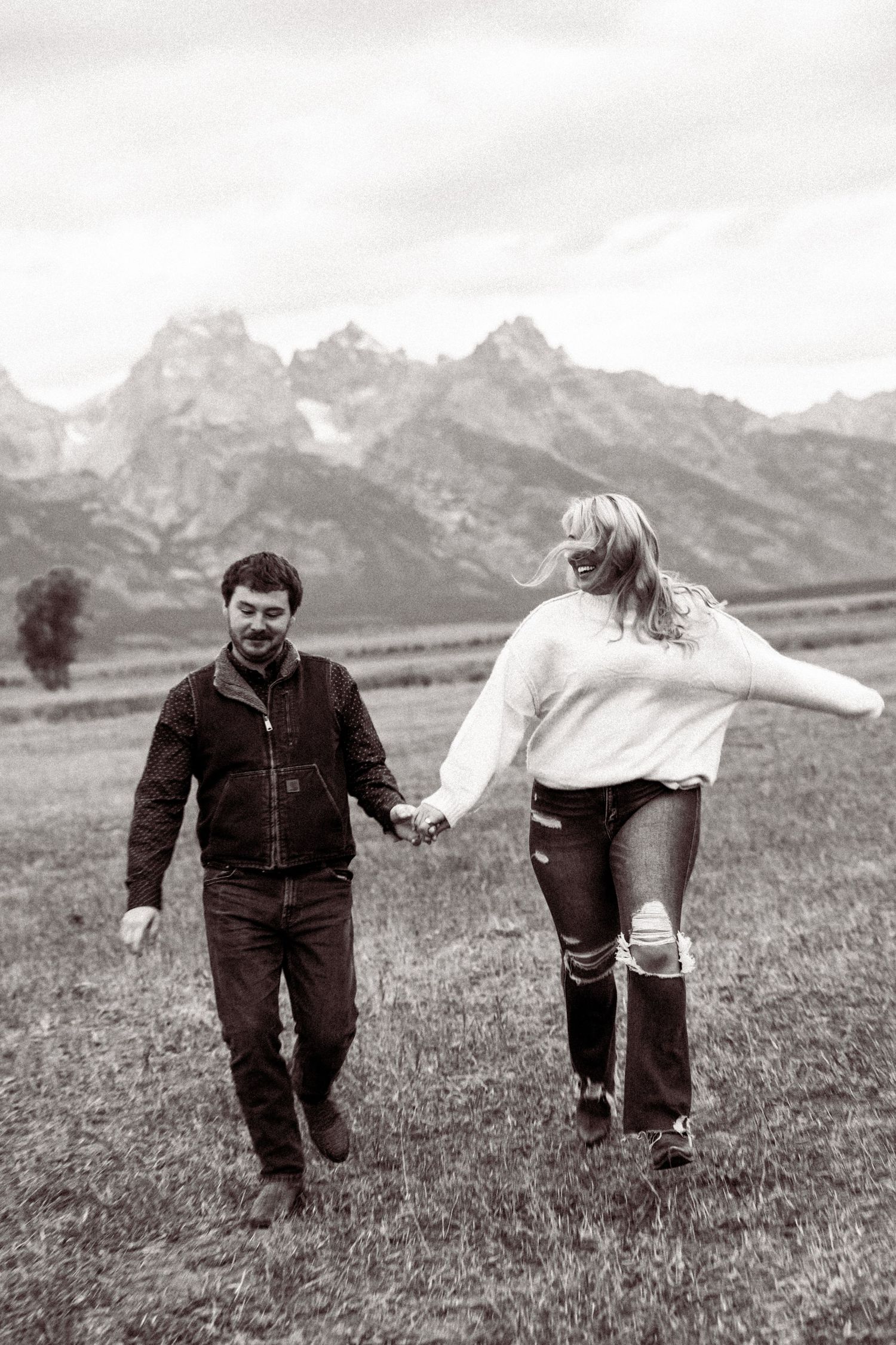 Black and white photos of a playful couple running and spinning in a mountain meadow.