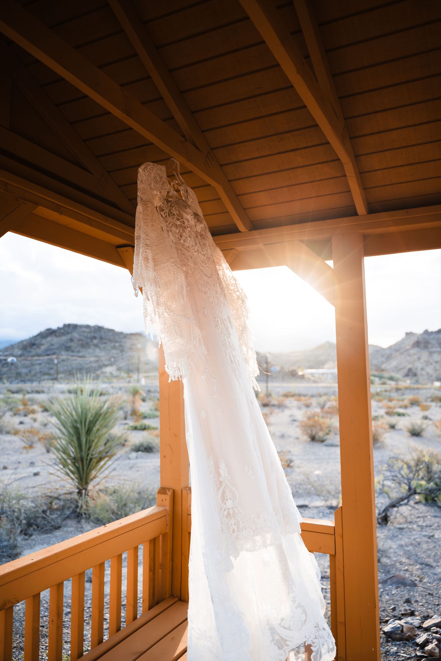Lace wedding dress hanging on wooden porch with desert mountain landscape in background.