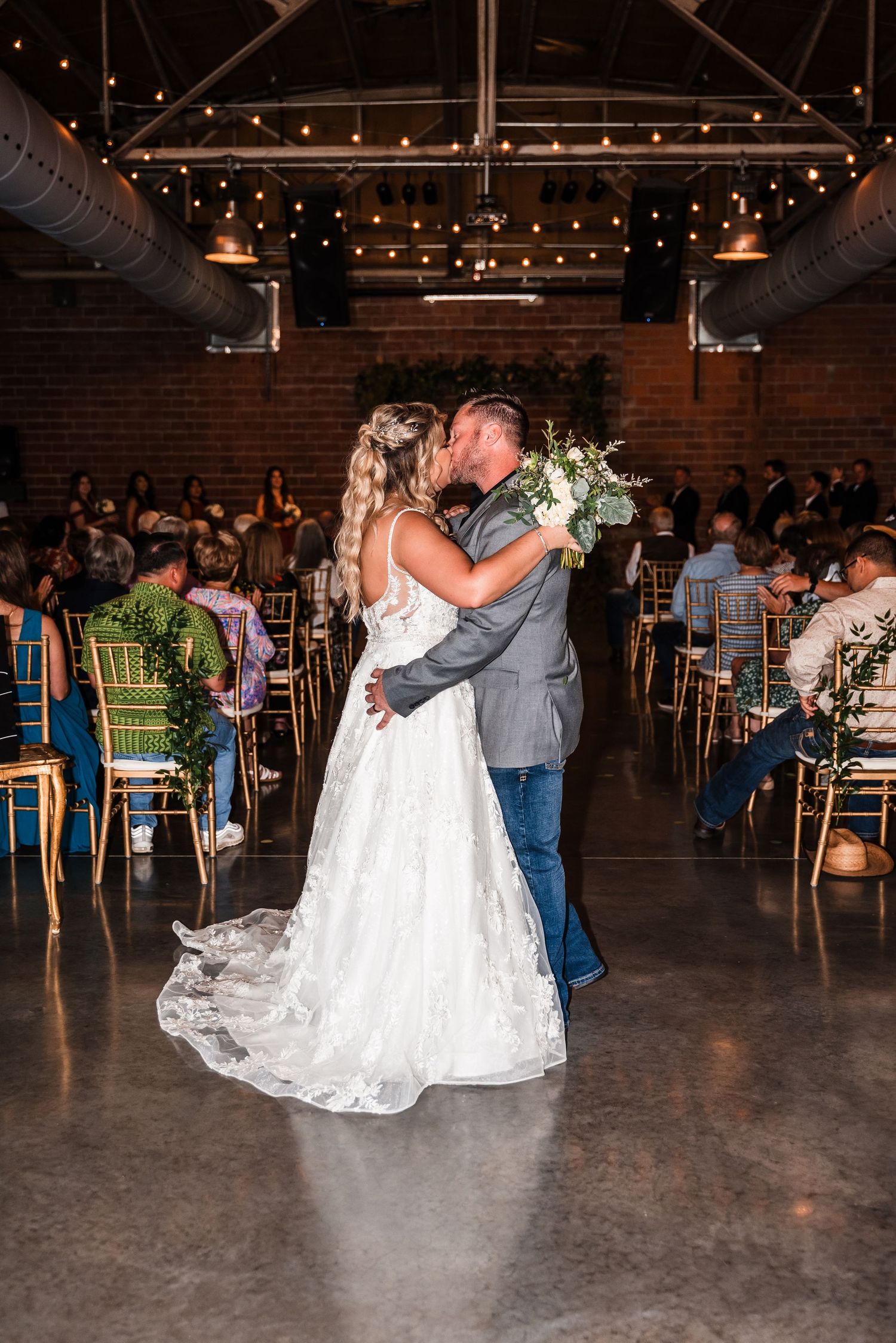 A couple celebrates their first dance at a rustic indoor wedding venue with string lights and exposed brick walls.
