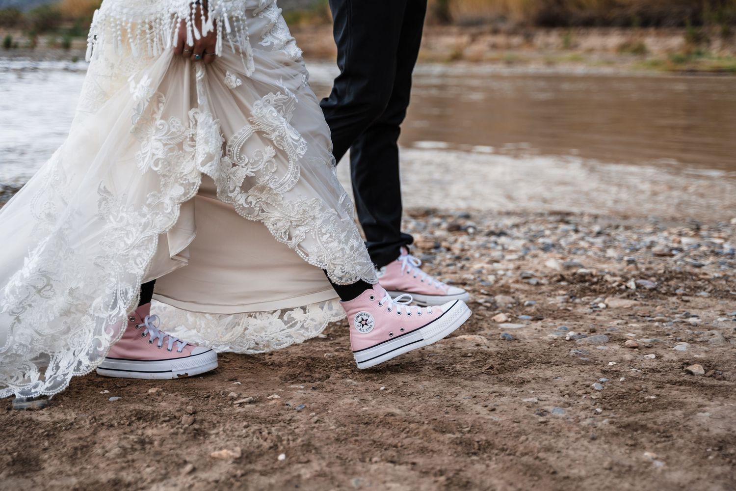 Close-up of bride and groom's feet wearing matching pink converse sneakers with lace dress detail.