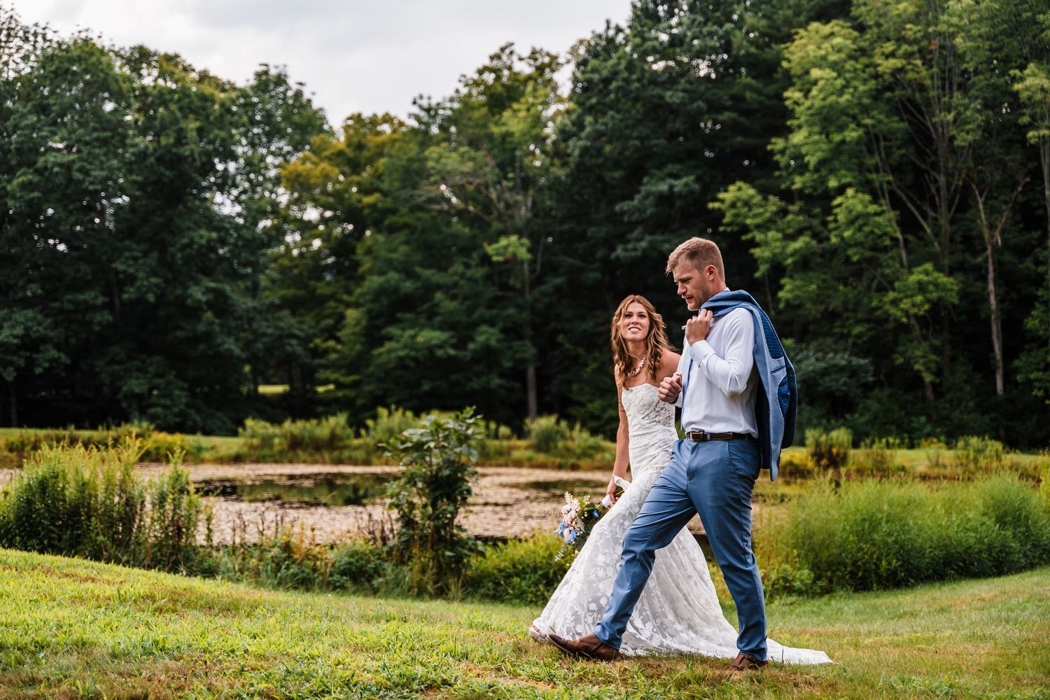 Two people walking together on a grassy hill during a wedding photo session.