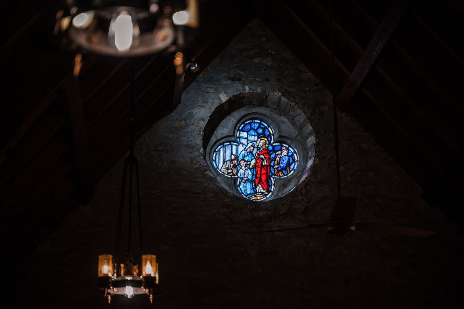 Stained glass window with a blue and red cross design illuminated inside a dark church.