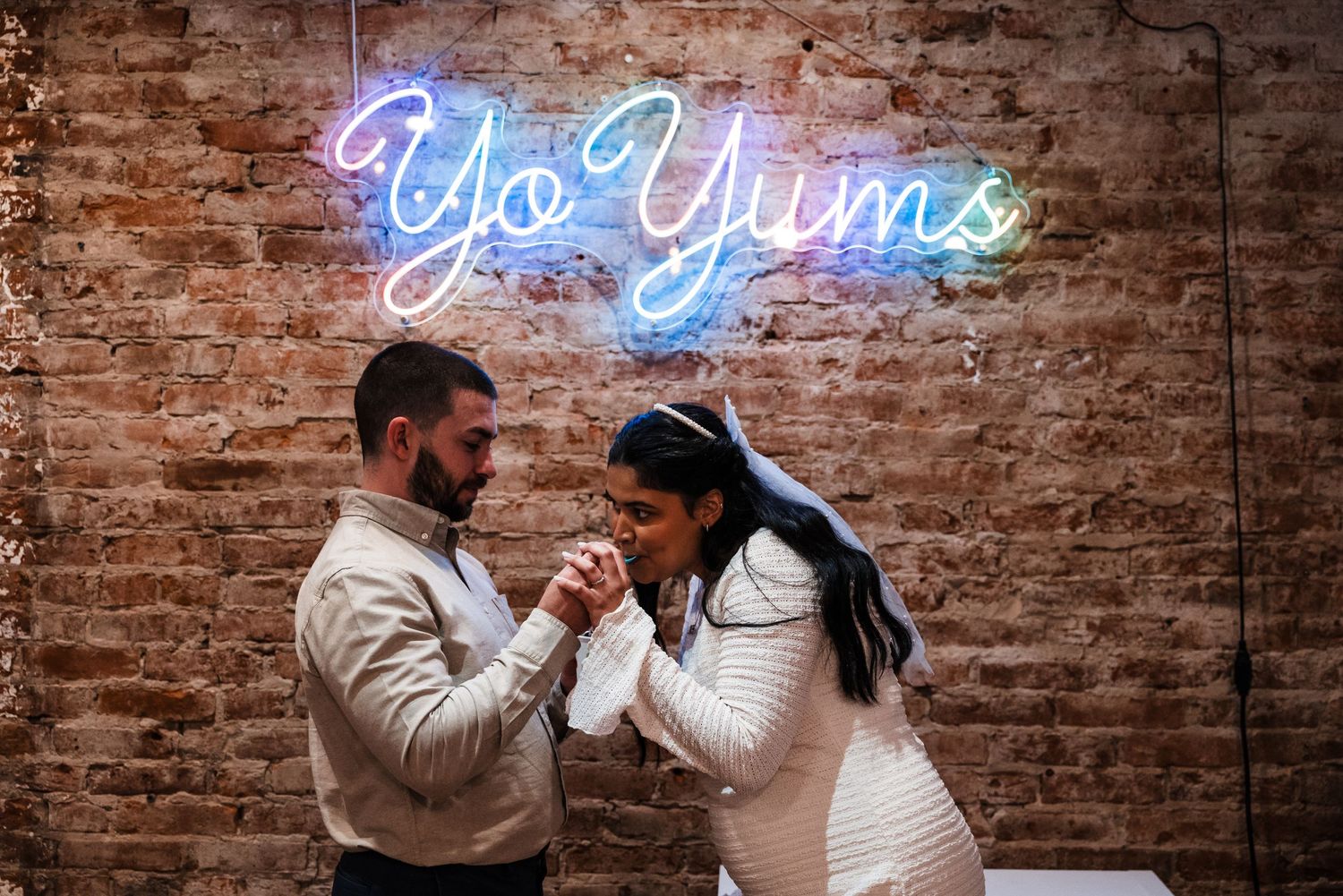Romantic moment between couple in front of neon sign on brick wall.