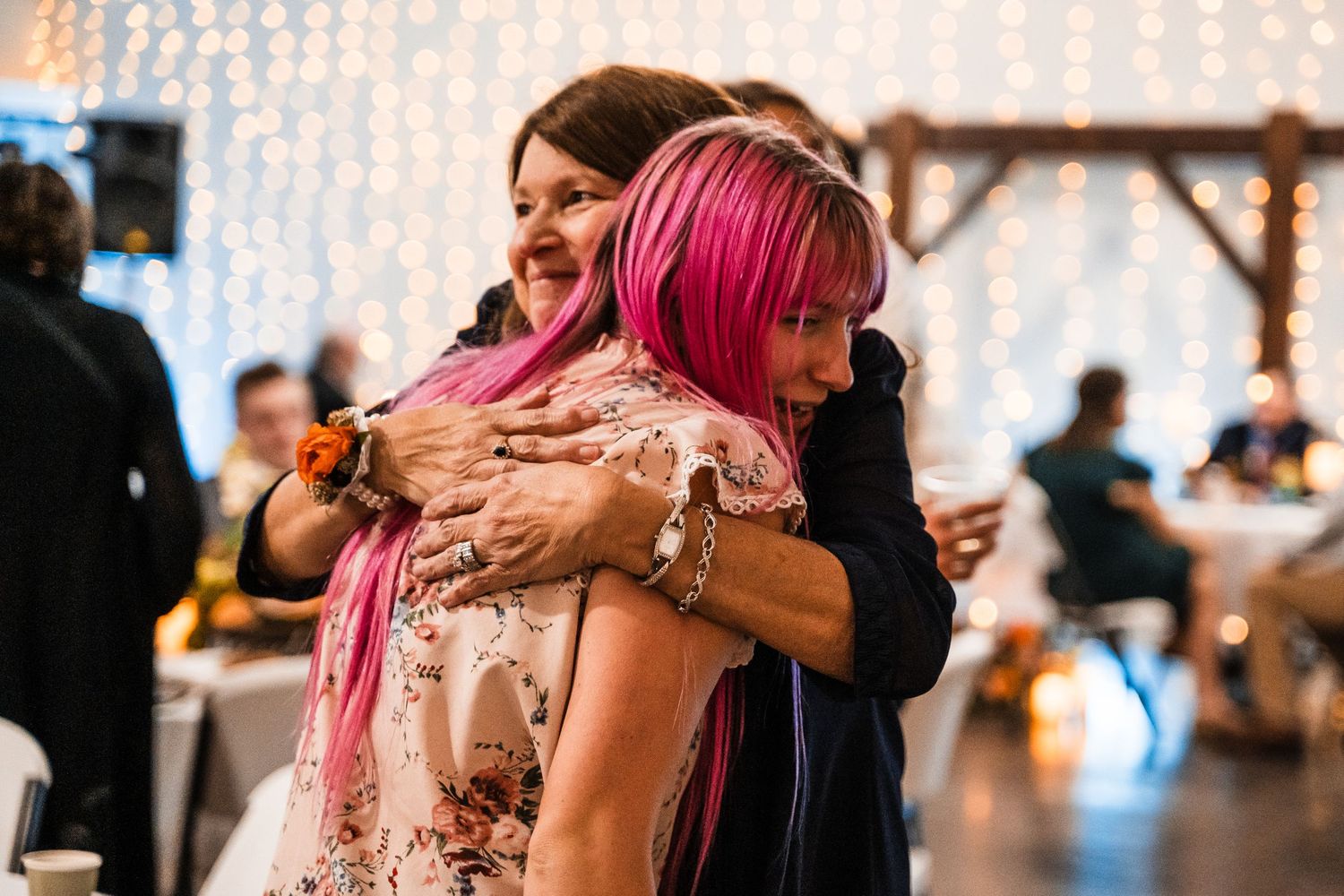Two guests embrace and celebrate on the dance floor with string lights in background.
