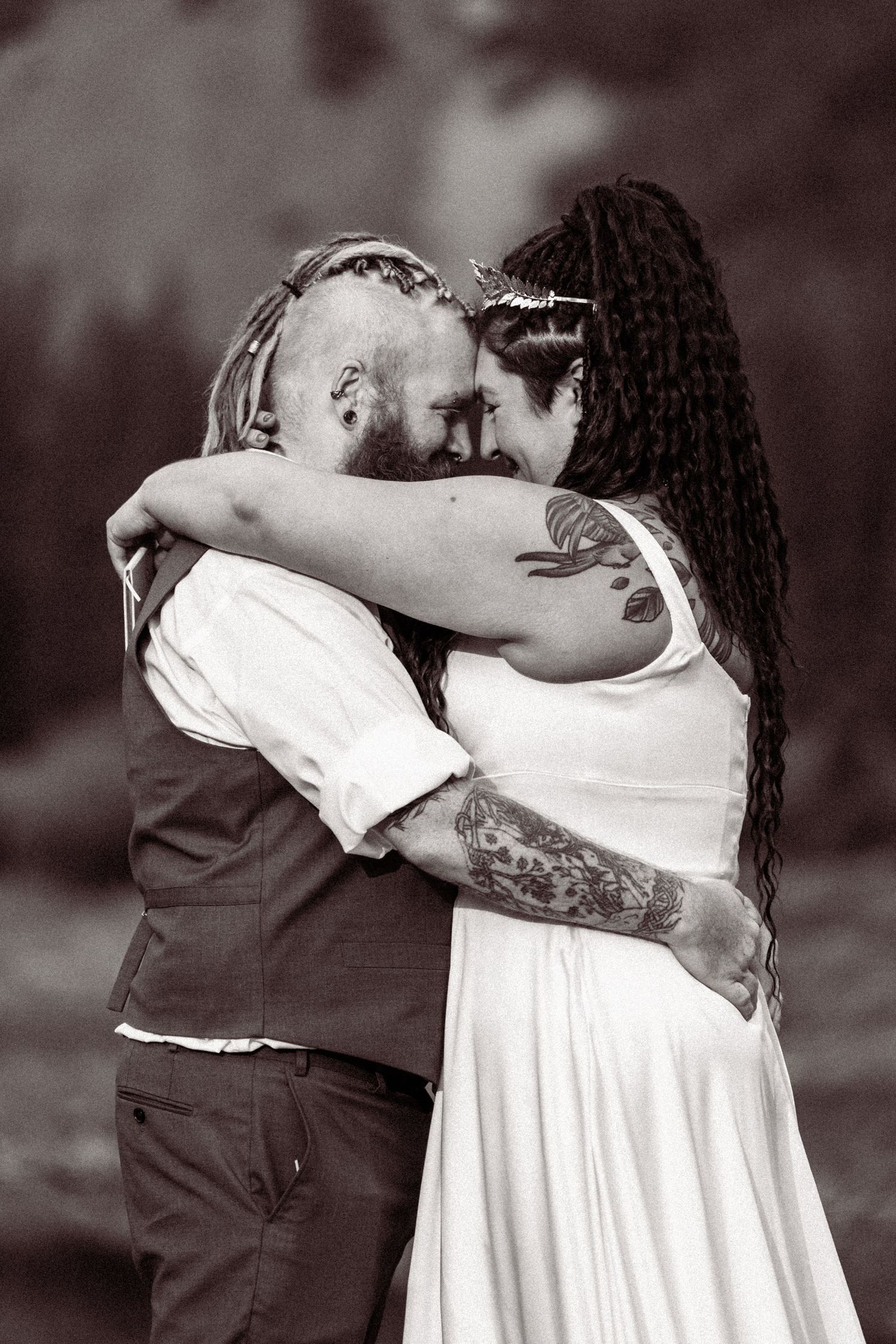 Tattooed couple shares an intimate embrace in black and white wedding photo with bride in white dress.