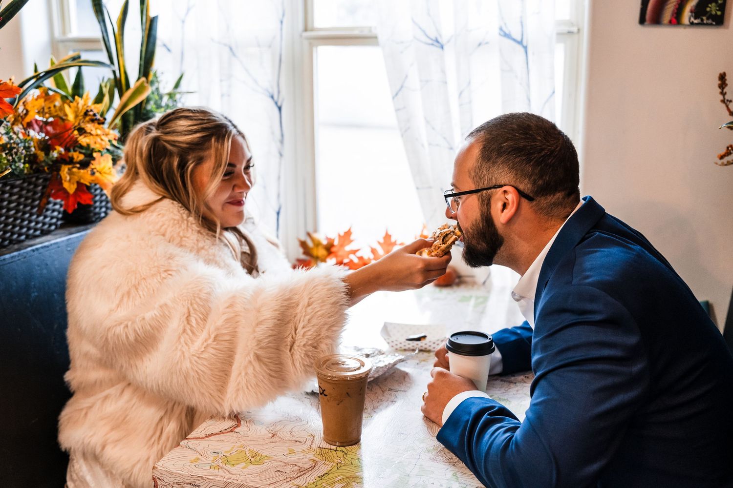 A couple in wedding attire shares an intimate moment while sitting together near a bright window.