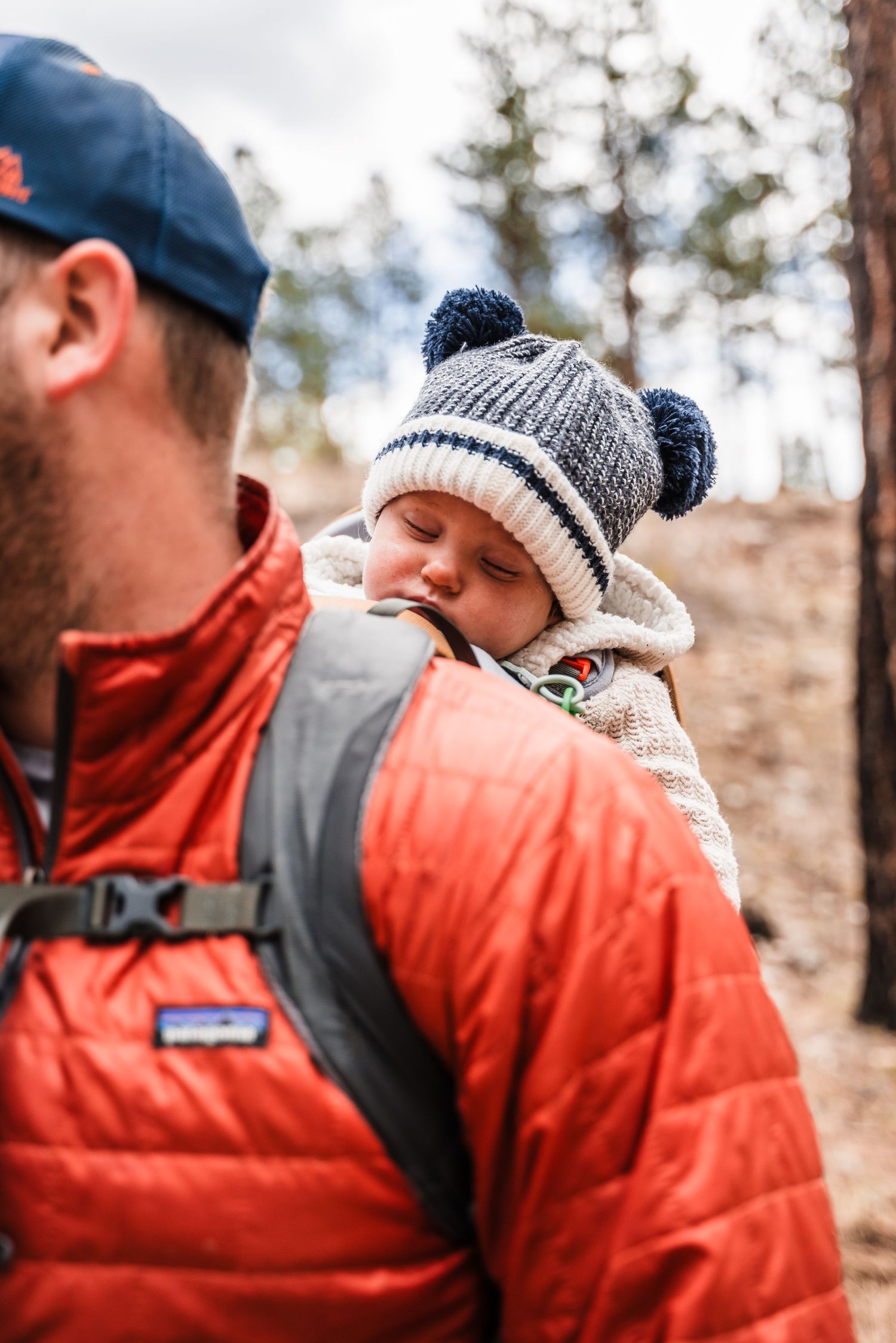A peaceful moment captured of a baby sleeping in a winter hat while being carried on a hiking trail.