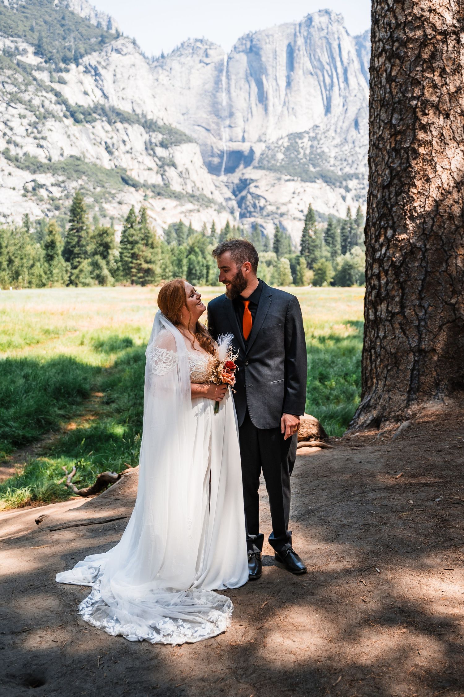A couple shares an intimate wedding moment in front of Yosemite's majestic granite cliffs on a sunny summer day.