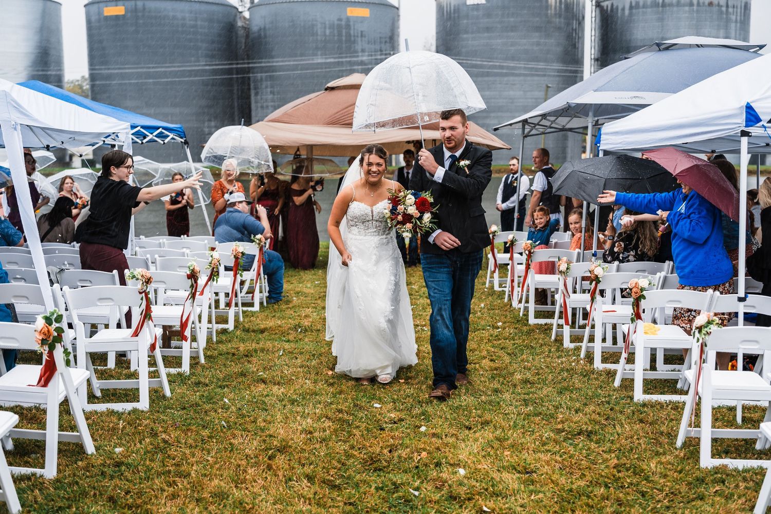 Wide view of an outdoor wedding setup with white chairs arranged on grass under white tents.