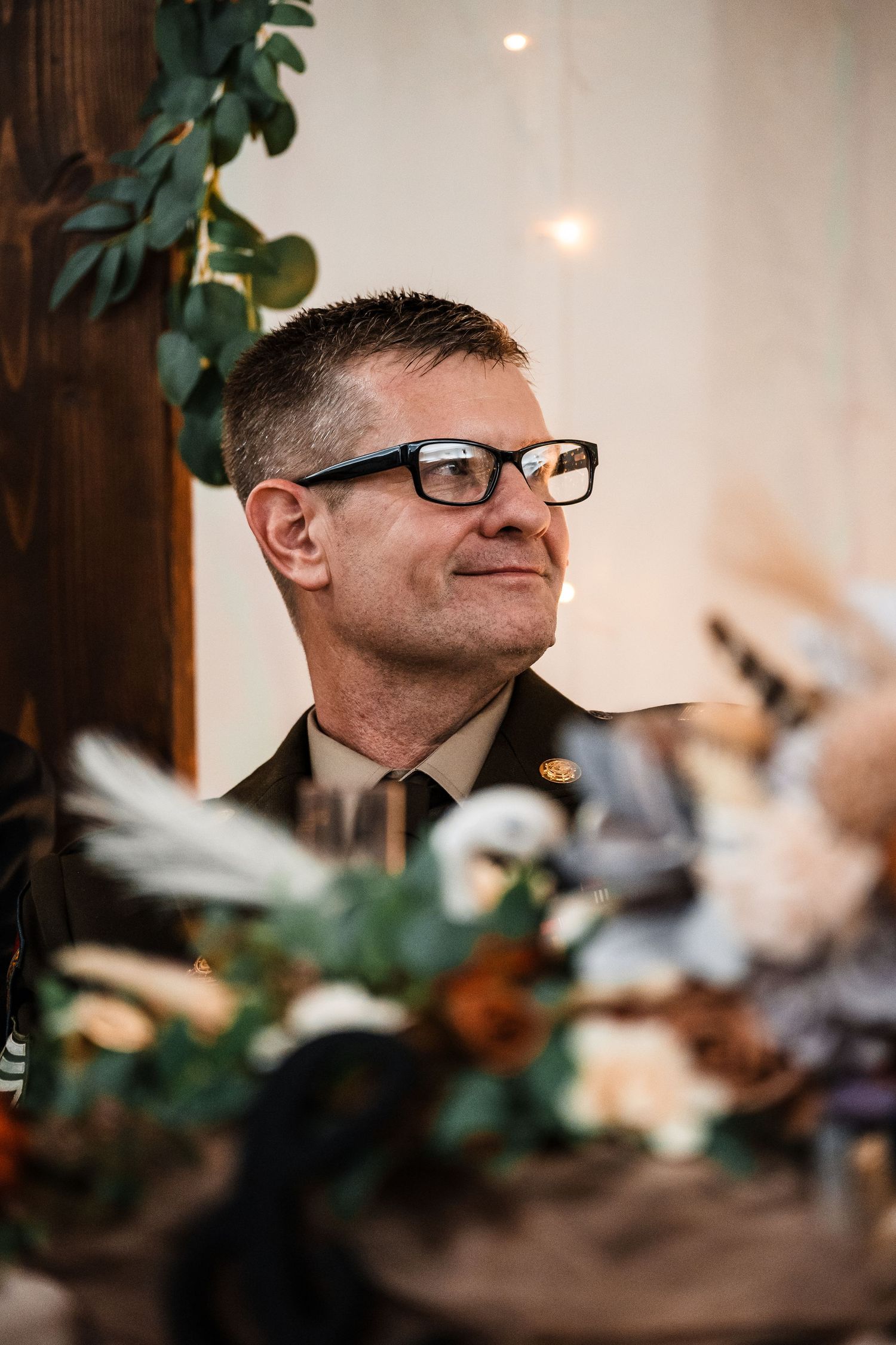 Close-up profile view of someone wearing glasses against a blurred background with string lights and greenery.
