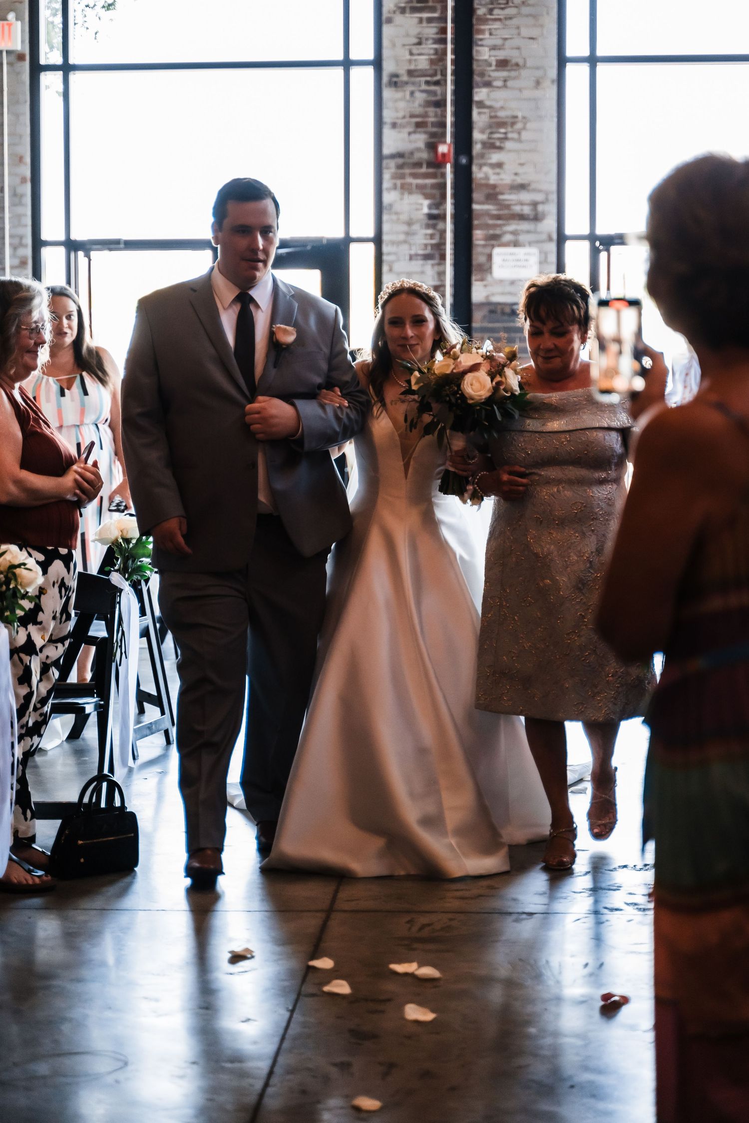 A traditional wedding processional in an industrial-style venue with exposed brick walls and large windows.