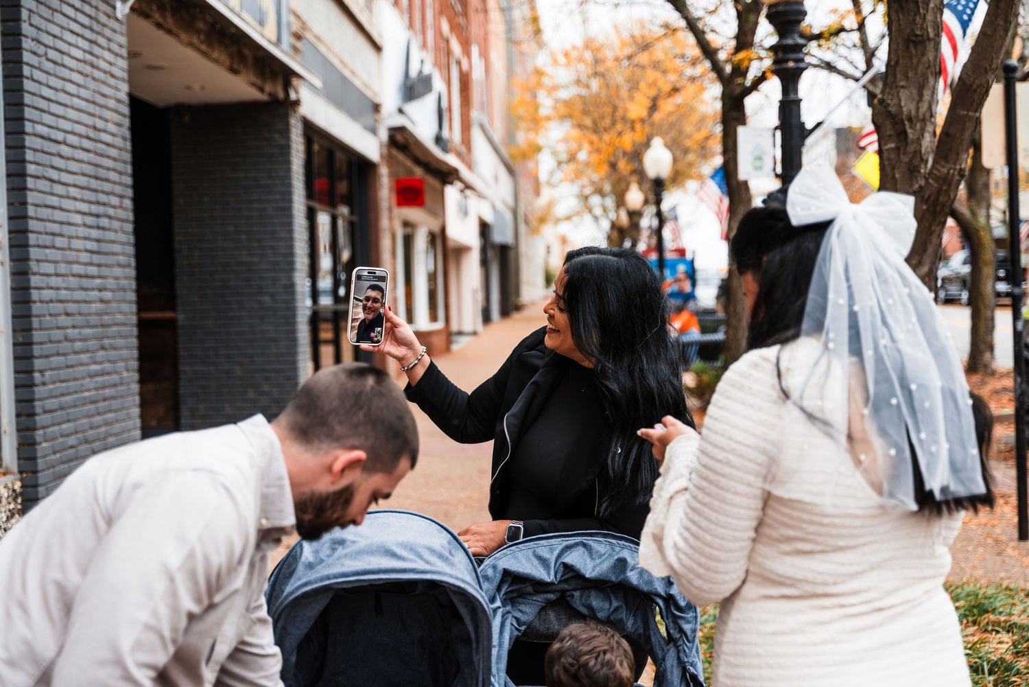 People gathered on an autumn sidewalk with brick buildings and fall foliage in the background.