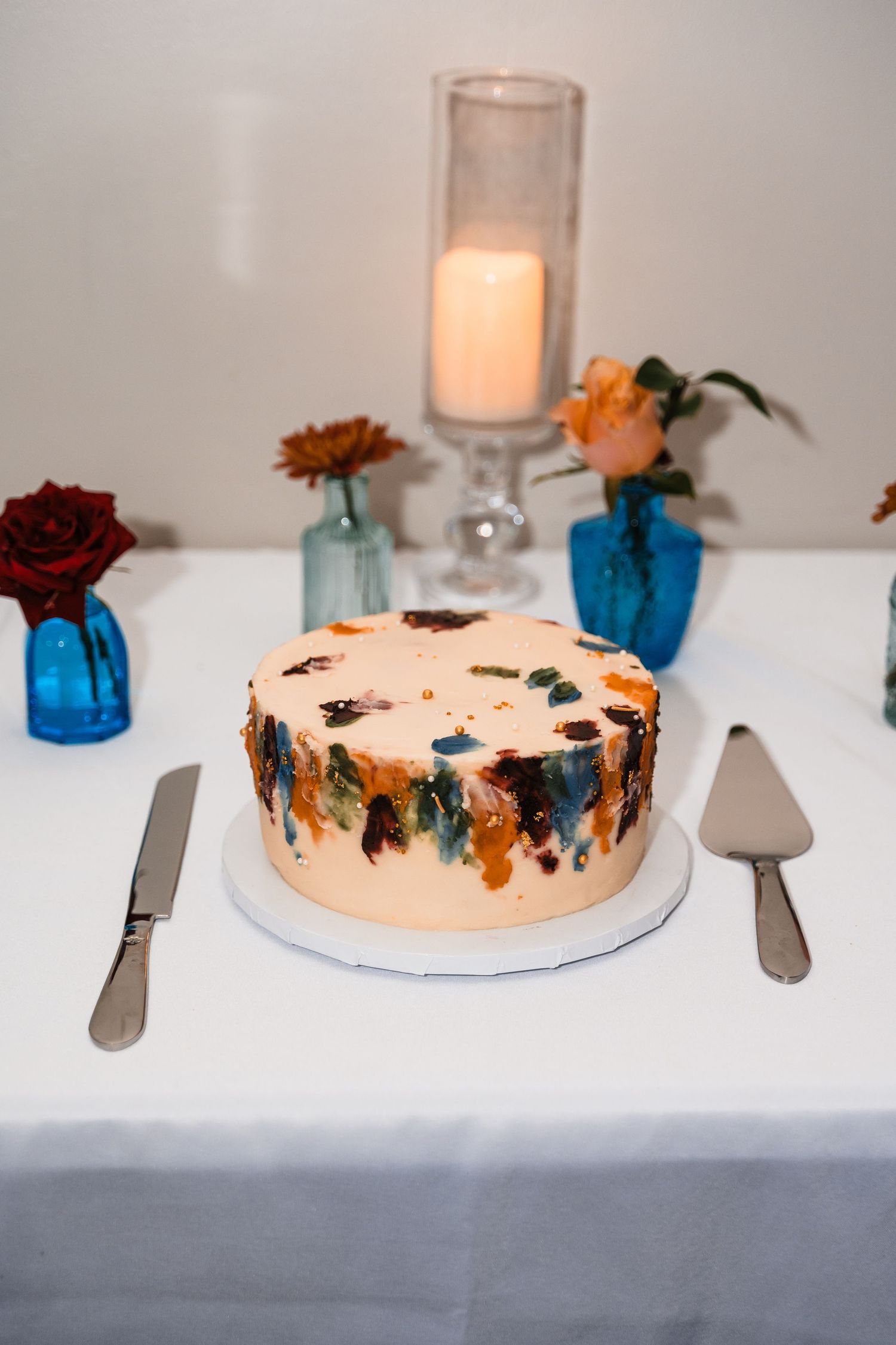 Wedding cake with abstract watercolor design in blue and orange surrounded by floral decor.