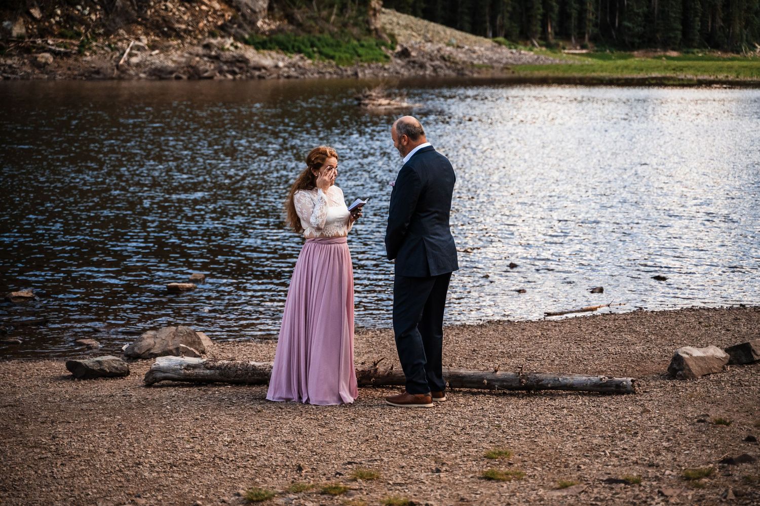 A lakeside ceremony scene with mountains and forest in the background.