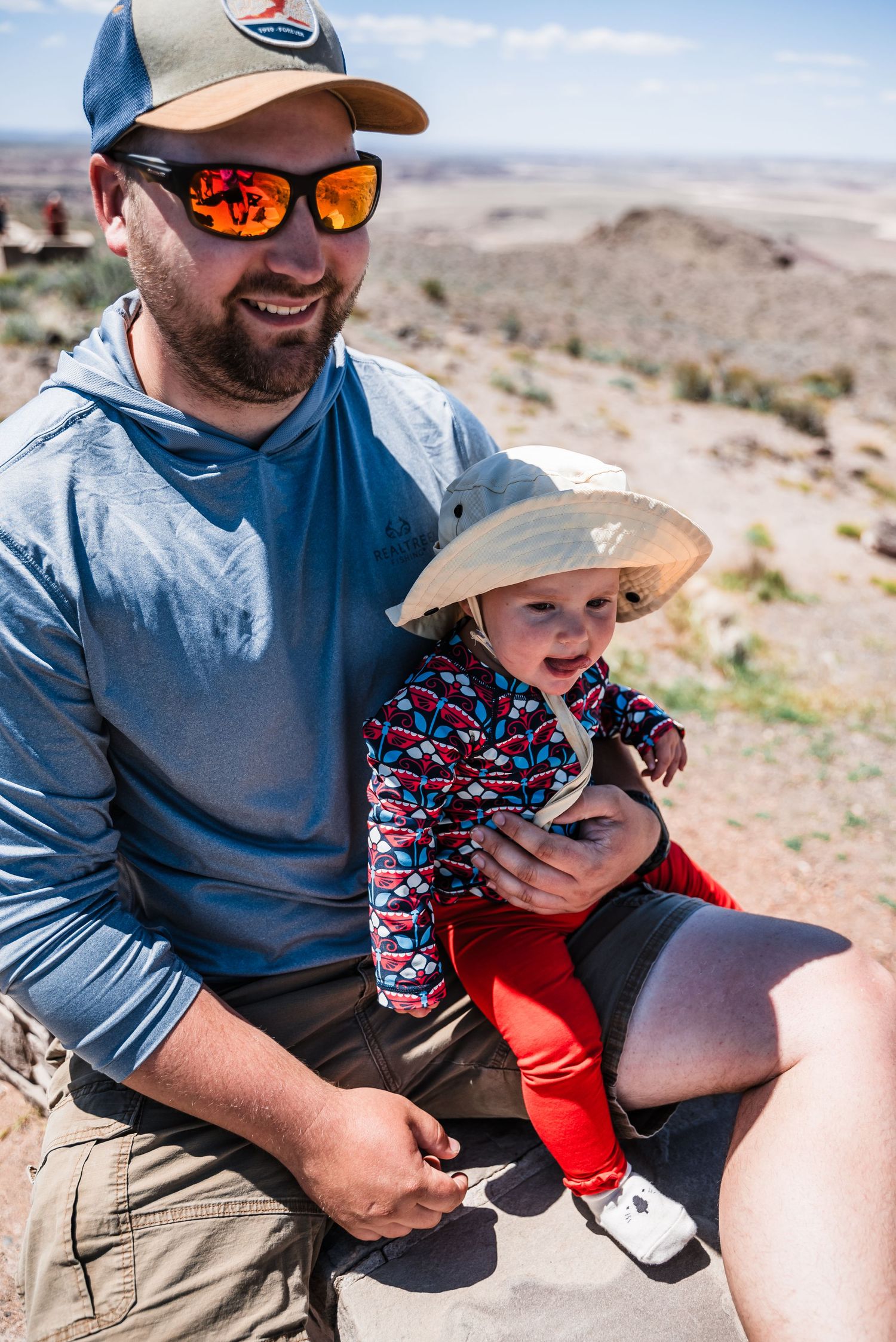 A pair enjoying a sunny day in the desert landscape while wearing sun protection gear.